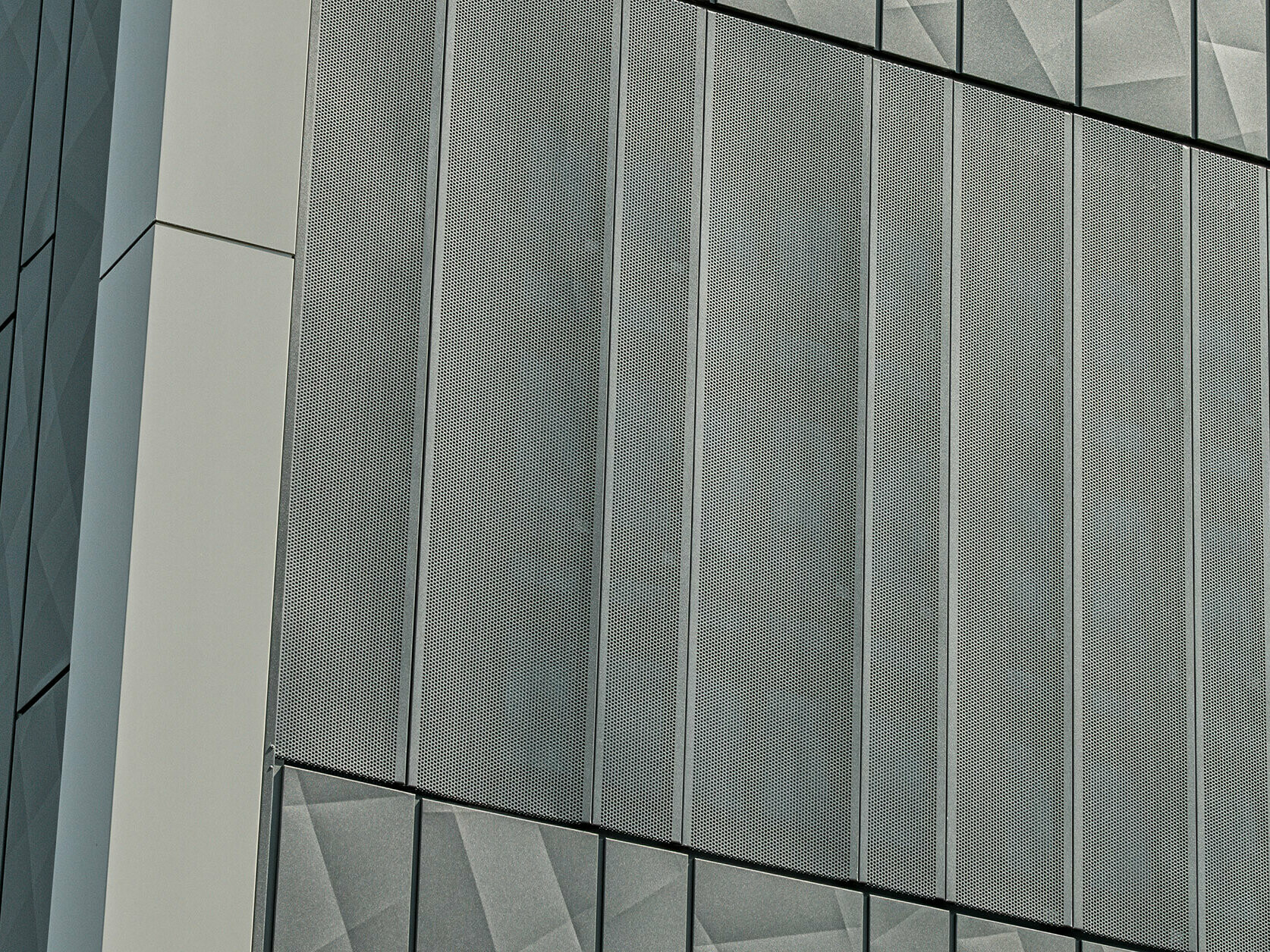 Vista della facciata di un negozio Eurospar a Rohrbach con rivestimento PREFA Siding.X e doghe perforate nel colore antracite. Gli elementi doga.X presentano un vivace disegno geometrico delle fughe, mentre le doghe perforate offrono una struttura moderna e traspirante.