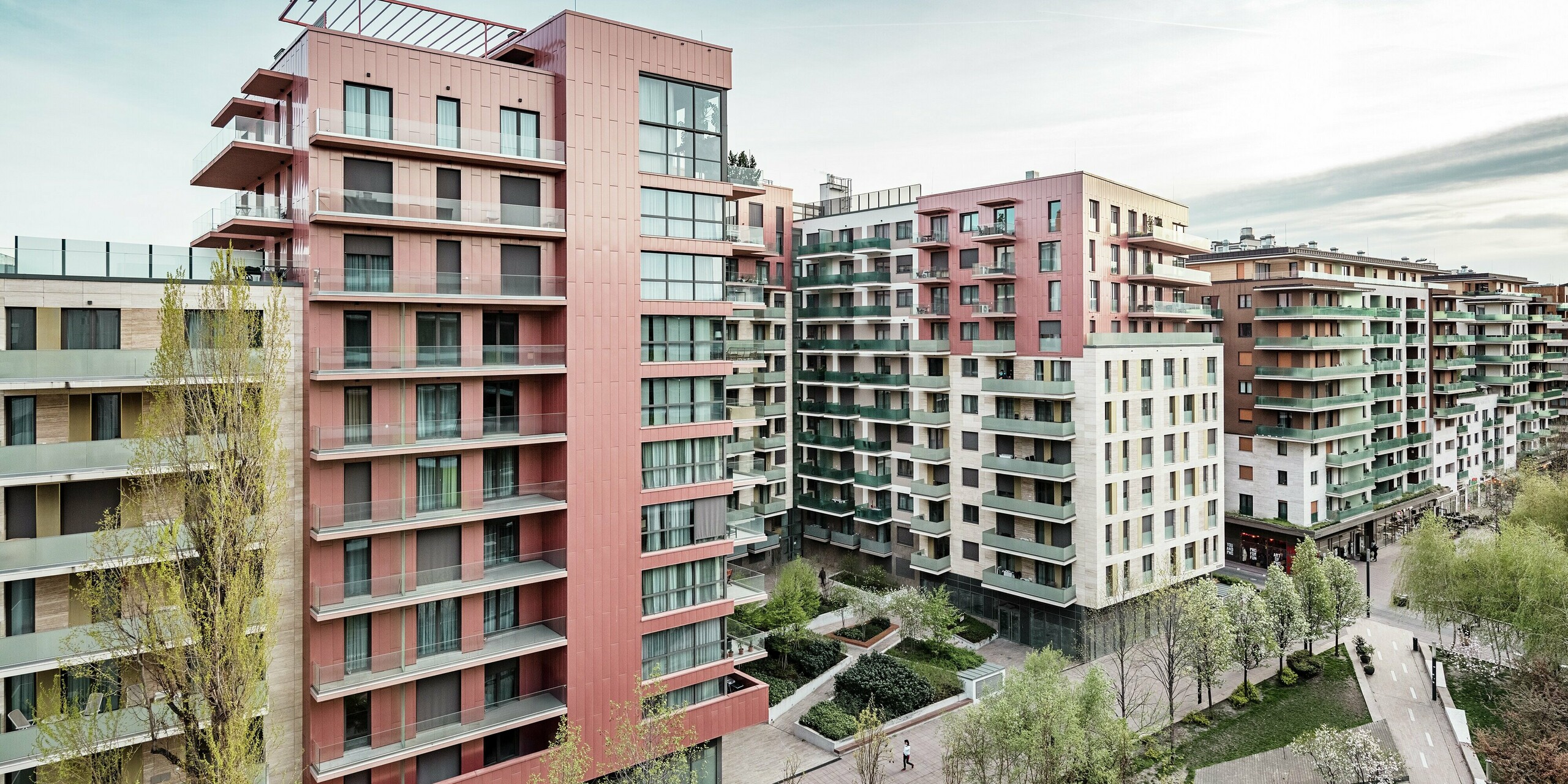 Panoramaaufnahme des Grand Corvin Wohnkomplexes im neugestalteten Corvin-Viertels in Budapest. Die markanten Gebäudeteile sind mit über 800 m² PREFA Siding Fassadenpaneelen in vertikaler Verlegung und Sonderfarbe Lachsmetallic versehen. Die langlebige Aluminiumverkleidung setzt architektonische Highlights, fügt sich harmonisch in die urbane Struktur ein und unterstreicht den hochwertigen, zeitgemäßen Charakter der neuen Wohnanlage entlang der Corvin-Promenade.