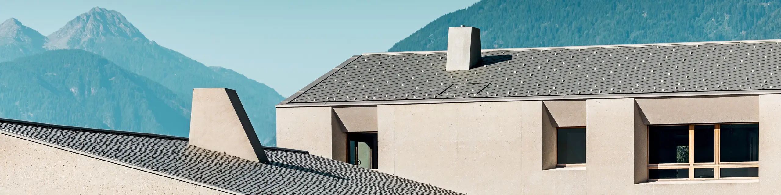 Il centro educativo di Riffian, in Alto Adige, crea un effetto di grande impatto sullo sfondo alpino grazie alle scaglie PREFA di dimensioni 44 × 44 e nel colore P.10 bronzo. Il tetto in alluminio, posato con precisione, si armonizza con la facciata dai toni tenui che ricordano l’argilla e sottolinea l’architettura moderna dell’asilo e della scuola elementare.