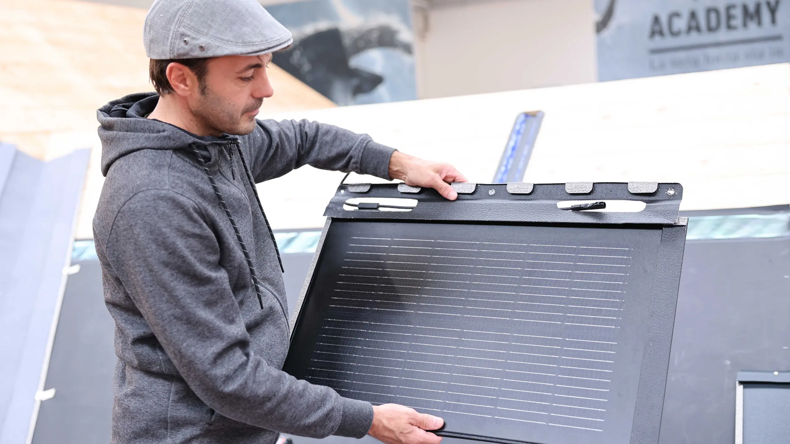 Ein Mitarbeiter der PREFA Academy in Italien zeigt eine Solardachplatte von PREFA. Er hält die Platte in den Händen und demonstriert deren Design und Befestigungsmöglichkeiten. Im Hintergrund sind Schulungsräume der Academy erkennbar.