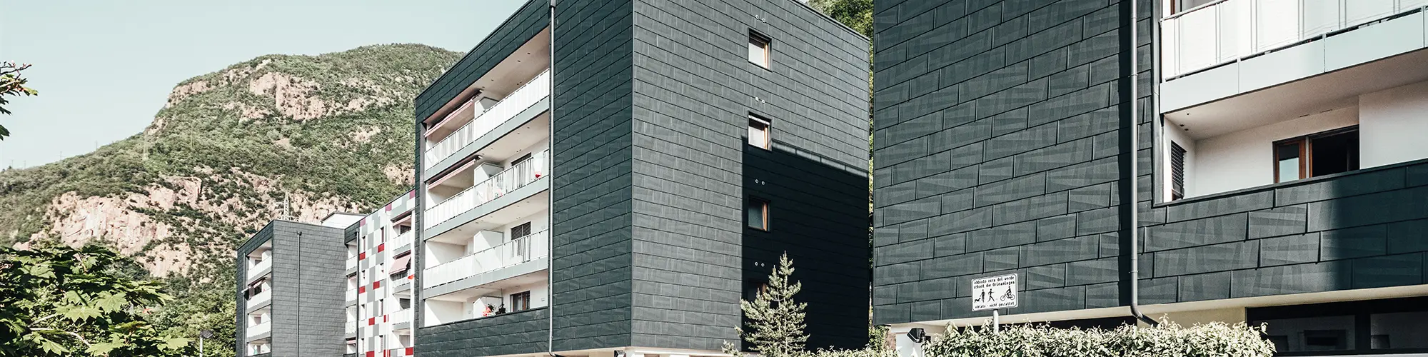 Ansicht von schräg vorne auf den sanierten Wohnbau in Bozen. Balkone mit weißem Geländer und Hausfassade realisiert mit dem Produkt Fassadenpaneel FX.12.