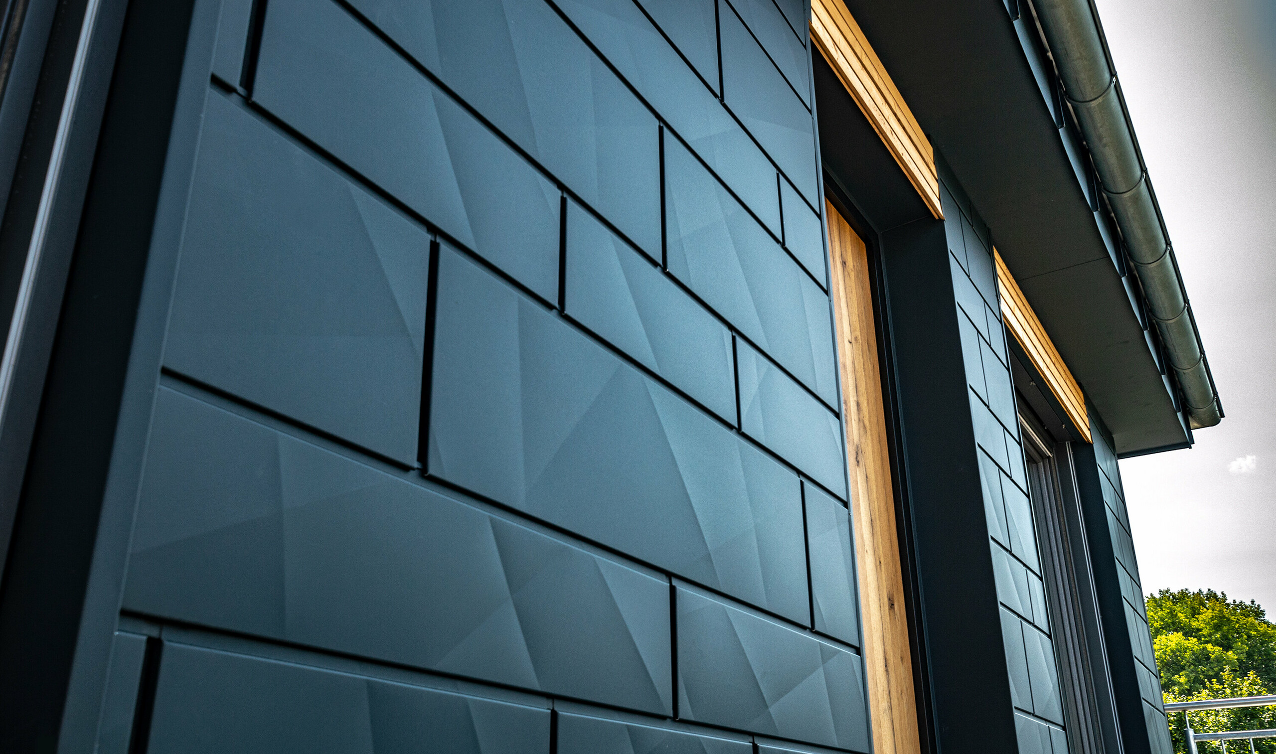 Fassade mit PREFA Siding.X in Anthrazit mit Balkontüren und großen Glasflächen gemischt mit einer Holzfassade.