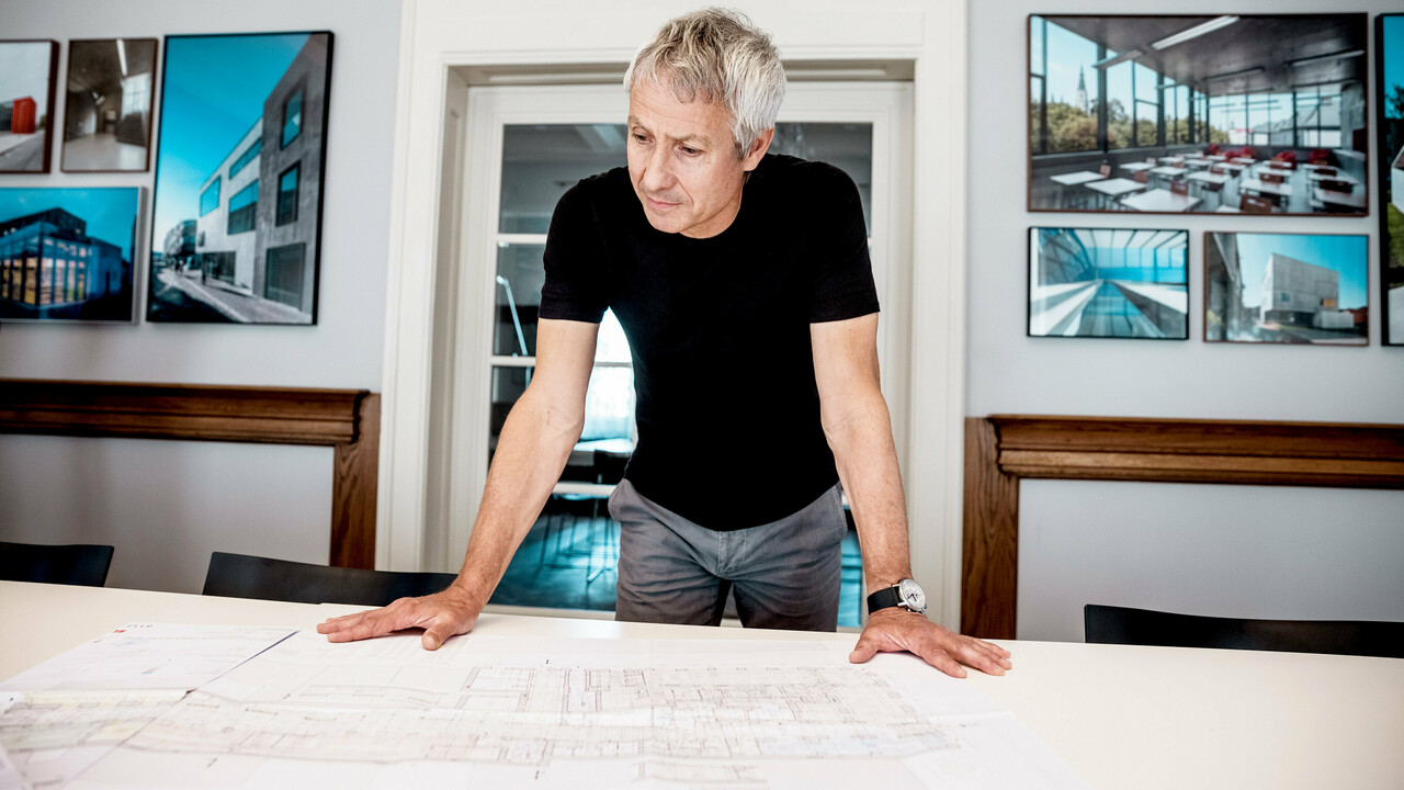 L'architetto lavora su progetti di costruzione dettagliati in un moderno ufficio, circondato da suggestive foto di progetti architettonici PREFA.