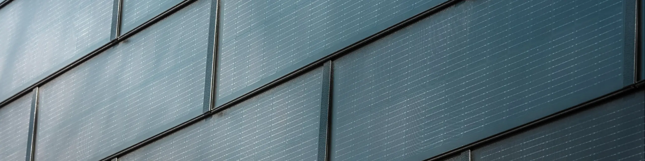 Primo piano di una facciata con tegole fotovoltaiche PREFA: i moduli fotovoltaici integrati nel sistema di facciata generano elettricità sostenibile e offrono un aspetto moderno ed estetico.