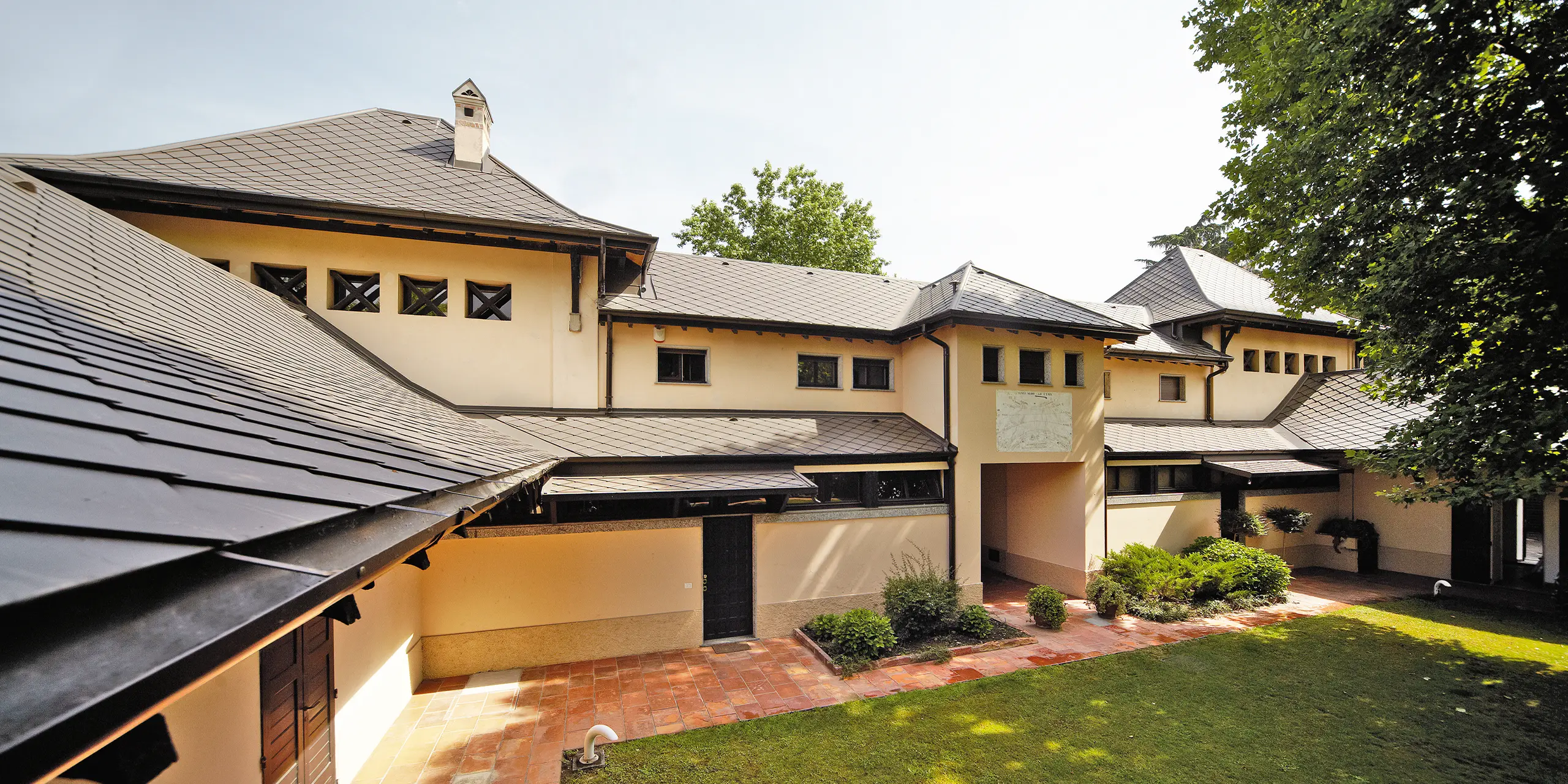 Villa italiana con tetto a scaglie in P.10 marrone di PREFA con facciata di color beige e cortile interno ombreggiato