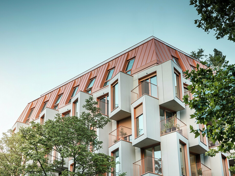 Moderna architettura residenziale nel progetto Van B a Monaco di Baviera, con un'innovativa facciata e il suggestivo tetto in alluminio PREFALZ nel colore speciale IGP Orange HDP di PREFA.  Il materiale di alta qualità del tetto convince per l'estrema durata, l'elevata resistenza e la solidità del colore. In combinazione con il design cubico della facciata e le ampie superfici vetrate, si crea un quadro d'insieme armonioso che combina funzionalità, design e sostenibilità ai massimi livelli, ideale per la vita urbana.