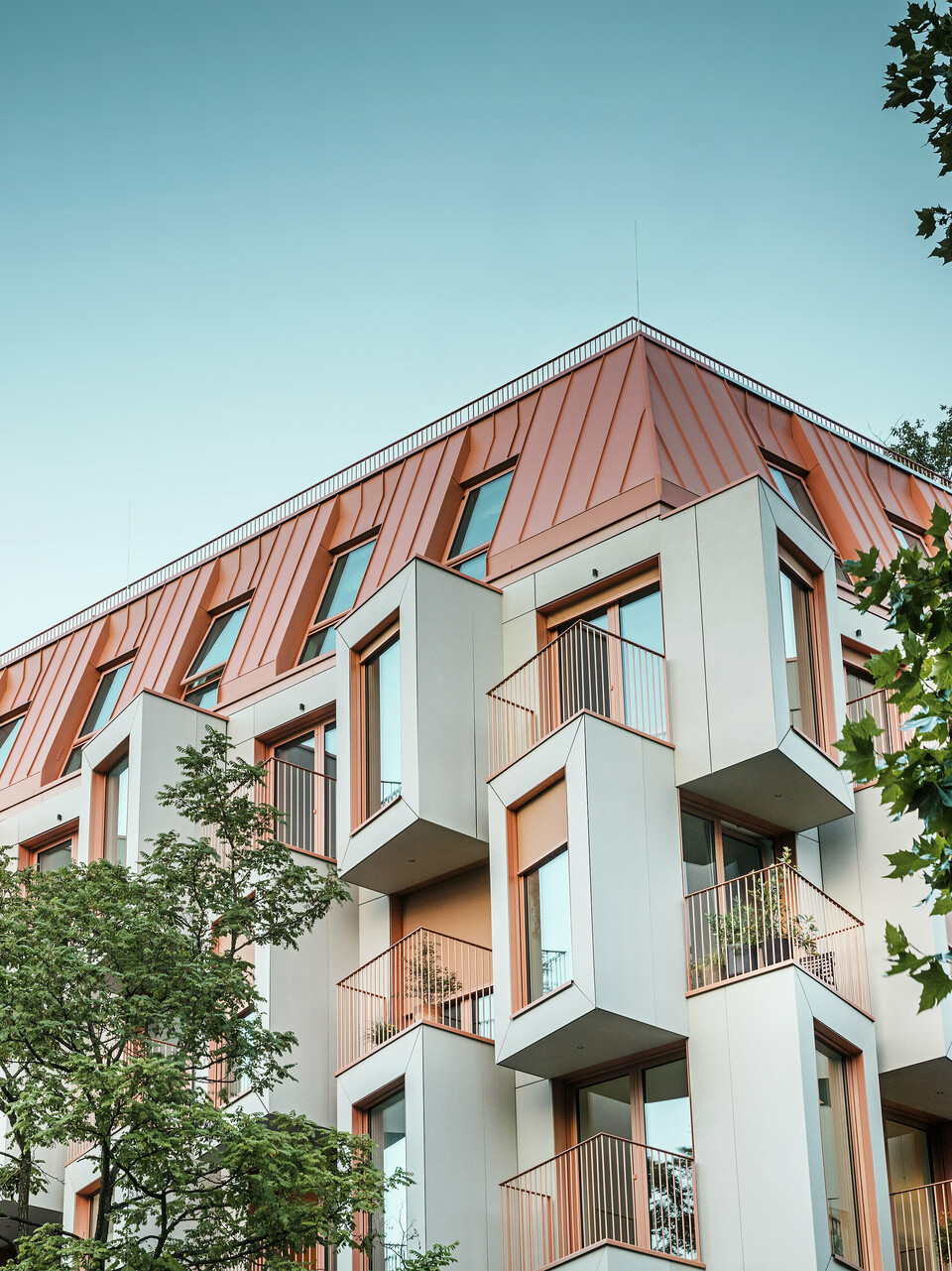 Moderne Wohnarchitektur im Projekt Van B in München mit einem innovativen Erker und einem markanten PREFALZ-Aluminiumdach in der Sonderfarbe IGP Orange HDP von PREFA. Das hochwertige Dachmaterial überzeugt durch seine außergewöhnliche Langlebigkeit, hohe Widerstandsfähigkeit und Farbstabilität. In Kombination mit der kubischen Fassadenform und den großflächigen Glasfronten entsteht ein harmonisches Gesamtbild, das Funktionalität, Design und Nachhaltigkeit auf höchstem Niveau vereint – ideal für urbanes Wohnen.