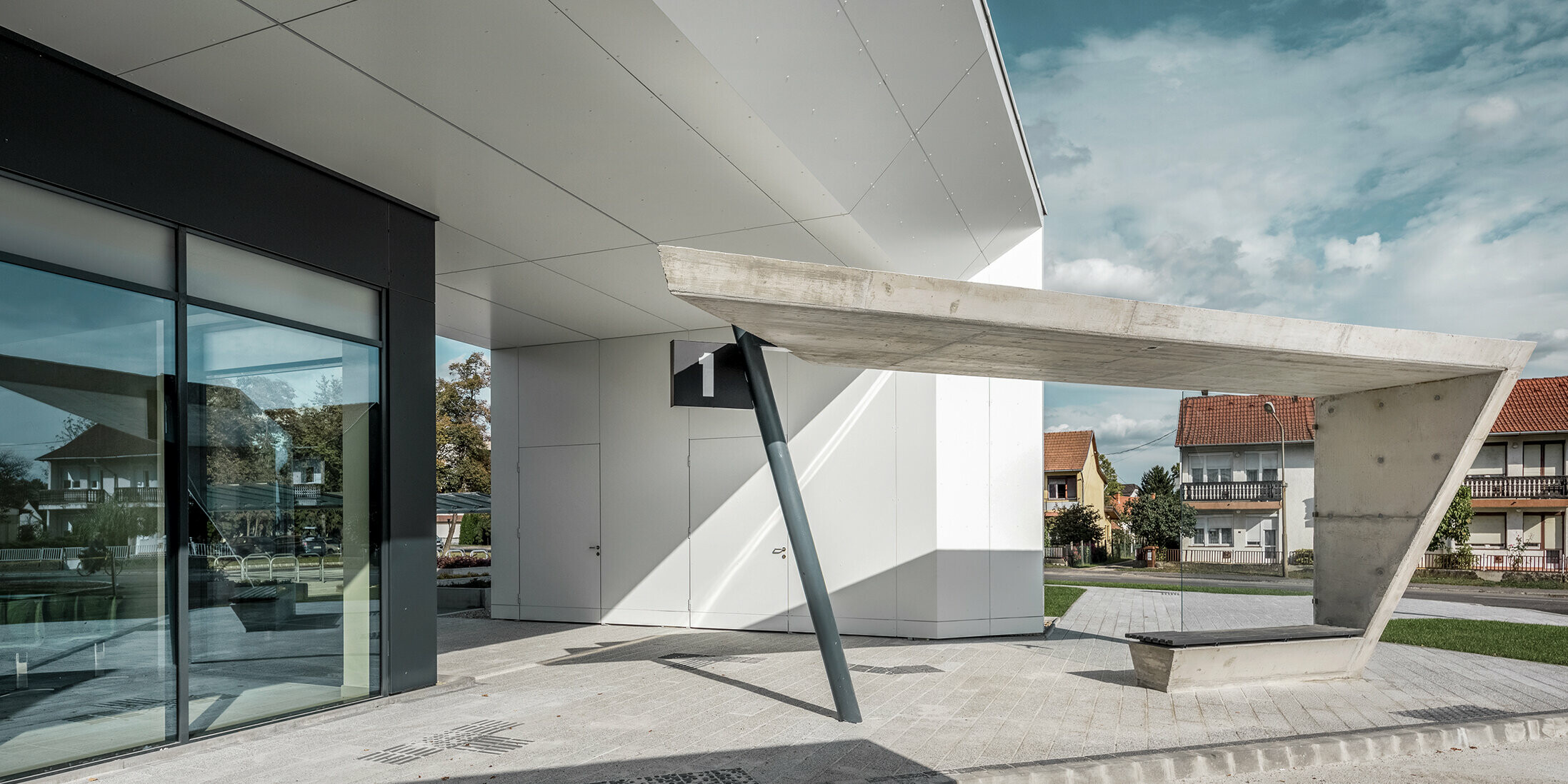 Eingangsbereich des Busbahnhofs Lenti; die Untersicht der Überdachung ist mit der PREFABOND Aluminium Verbundplatte von PREFA in Reinweiß verkleidet, die Fassadenelemente bei den Eingangstüren und Schaufenstern ist in P.10 anthrazit verkleidet.