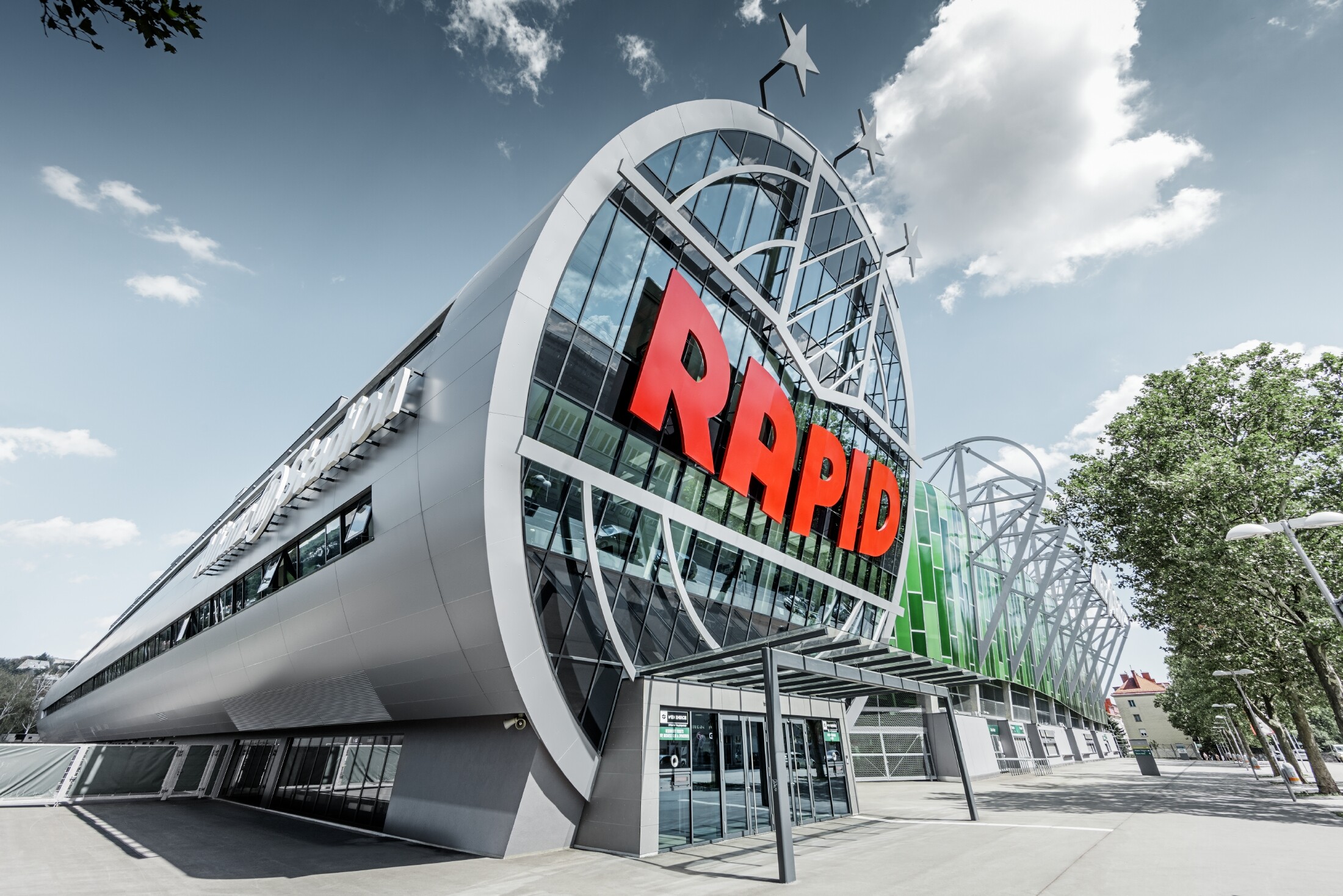 Ingresso all'Allianz Stadion con il grande logo SK Rapid Wien; il tubo con l’ampio frontale in vetro è rivestito con il pannello composito in alluminio PREFA in silver metallizzato.