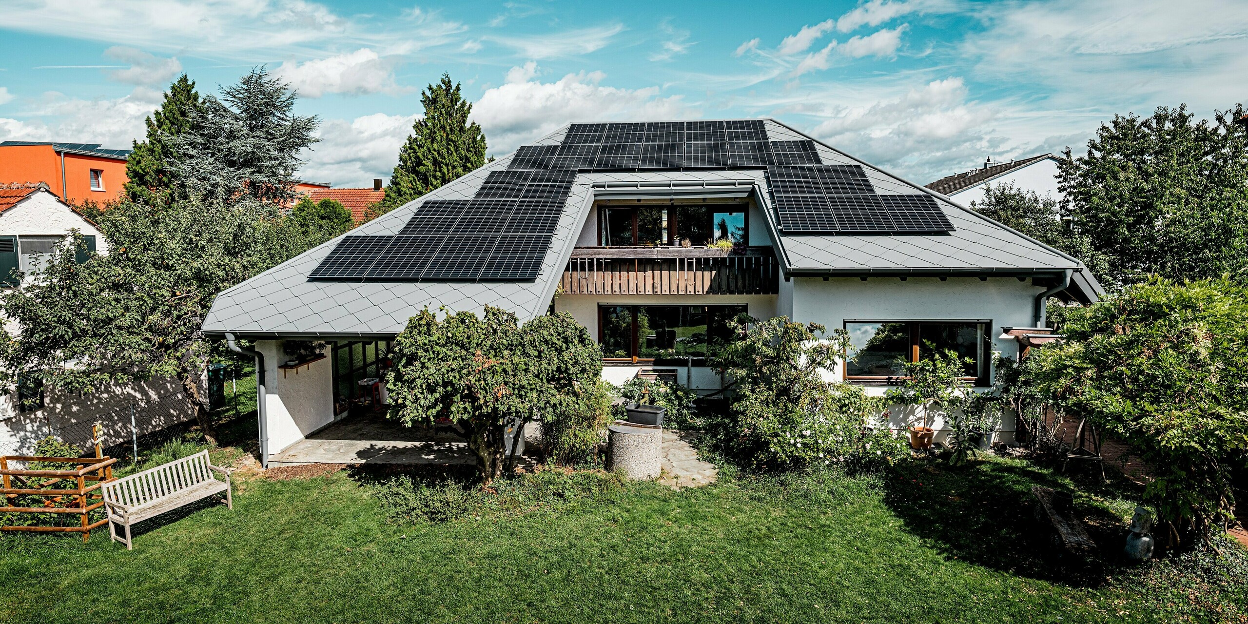 Das Bild zeigt die Rückseite eines Einfamilienhauses mit großem Garten, über dem das markante Walmdach mit PREFA Dachrauten 44 × 44 in P.10 Hellgrau dominiert. Die weitläufig montierte Photovoltaikanlage wirkt kraftvoll und modern und ist perfekt in das PREFA Aluminiumdach integriert. Die klaren Linien, die widerstandsfähige Rautenstruktur und die präzise Ausführung verleihen dem Gebäude ein hochwertiges Erscheinungsbild. Die robuste PREFA Dachlösung bietet maximale Stabilität und ideale Voraussetzungen für nachhaltige Energiegewinnung.