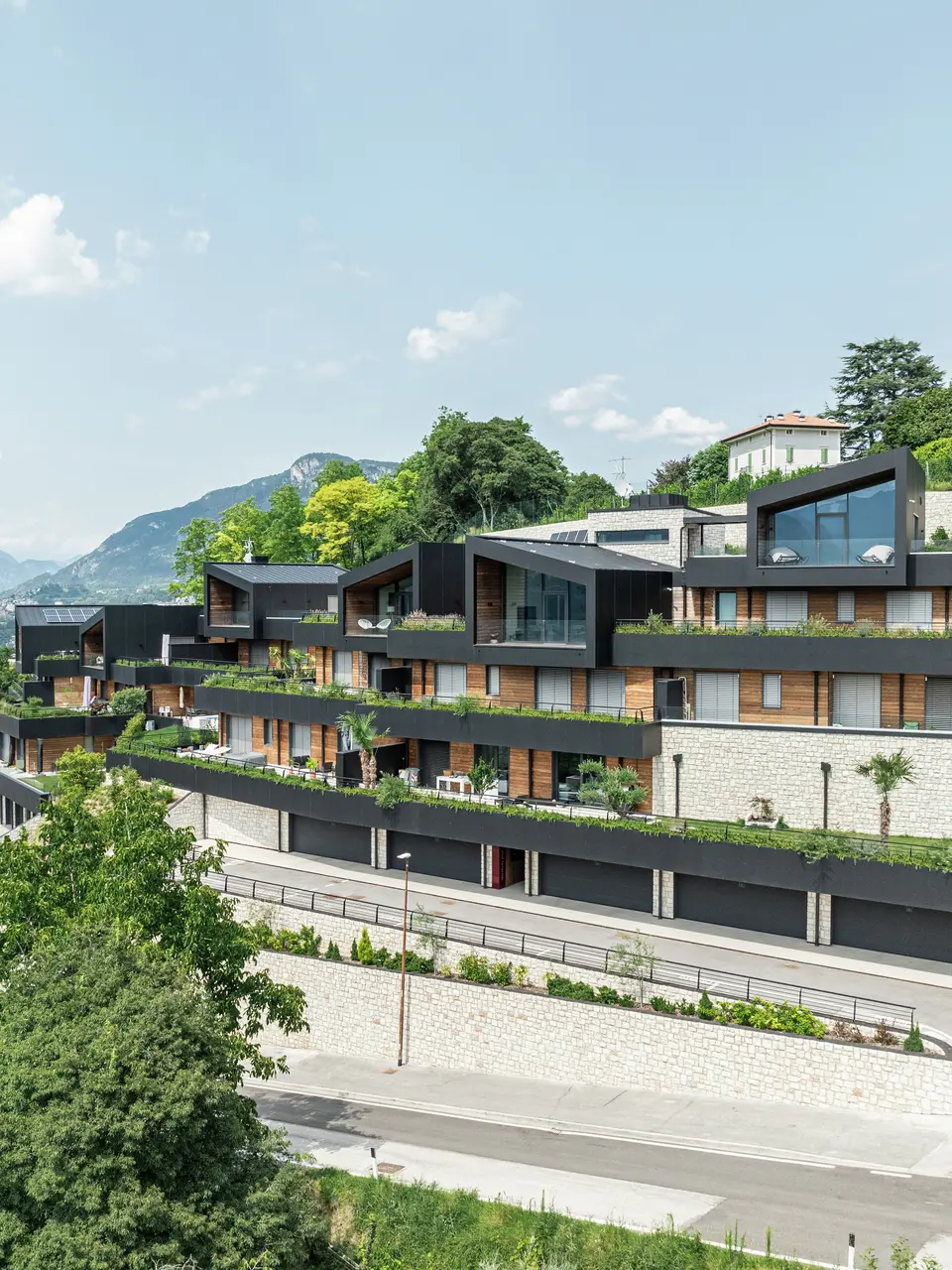 Die Wohnanlage fügt sich perfekt in die Hanglage oberhalb von Trient ein und bietet einen beeindruckenden Panoramablick auf die Stadt und die umliegende Berglandschaft. Die Kombination aus Naturstein, Holz und der hochwertigen PREFA Aluminiumfassade in P.10 Schwarz sorgt für ein modernes, elegantes Erscheinungsbild mit höchster Witterungsbeständigkeit. Das PREFALZ Dach in P.10 Schwarz garantiert Langlebigkeit und Schutz. Großzügige Terrassen mit gepflegter Bepflanzung unterstreichen das nachhaltige Wohnkonzept und schaffen ein harmonisches Zusammenspiel von Architektur und Natur.