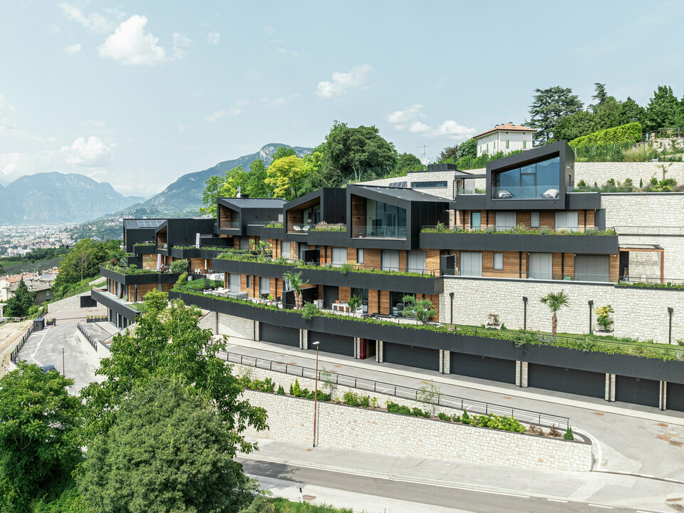 Die Wohnanlage fügt sich perfekt in die Hanglage oberhalb von Trient ein und bietet einen beeindruckenden Panoramablick auf die Stadt und die umliegende Berglandschaft. Die Kombination aus Naturstein, Holz und der hochwertigen PREFA Aluminiumfassade in P.10 Schwarz sorgt für ein modernes, elegantes Erscheinungsbild mit höchster Witterungsbeständigkeit. Das PREFALZ Dach in P.10 Schwarz garantiert Langlebigkeit und Schutz. Großzügige Terrassen mit gepflegter Bepflanzung unterstreichen das nachhaltige Wohnkonzept und schaffen ein harmonisches Zusammenspiel von Architektur und Natur.
