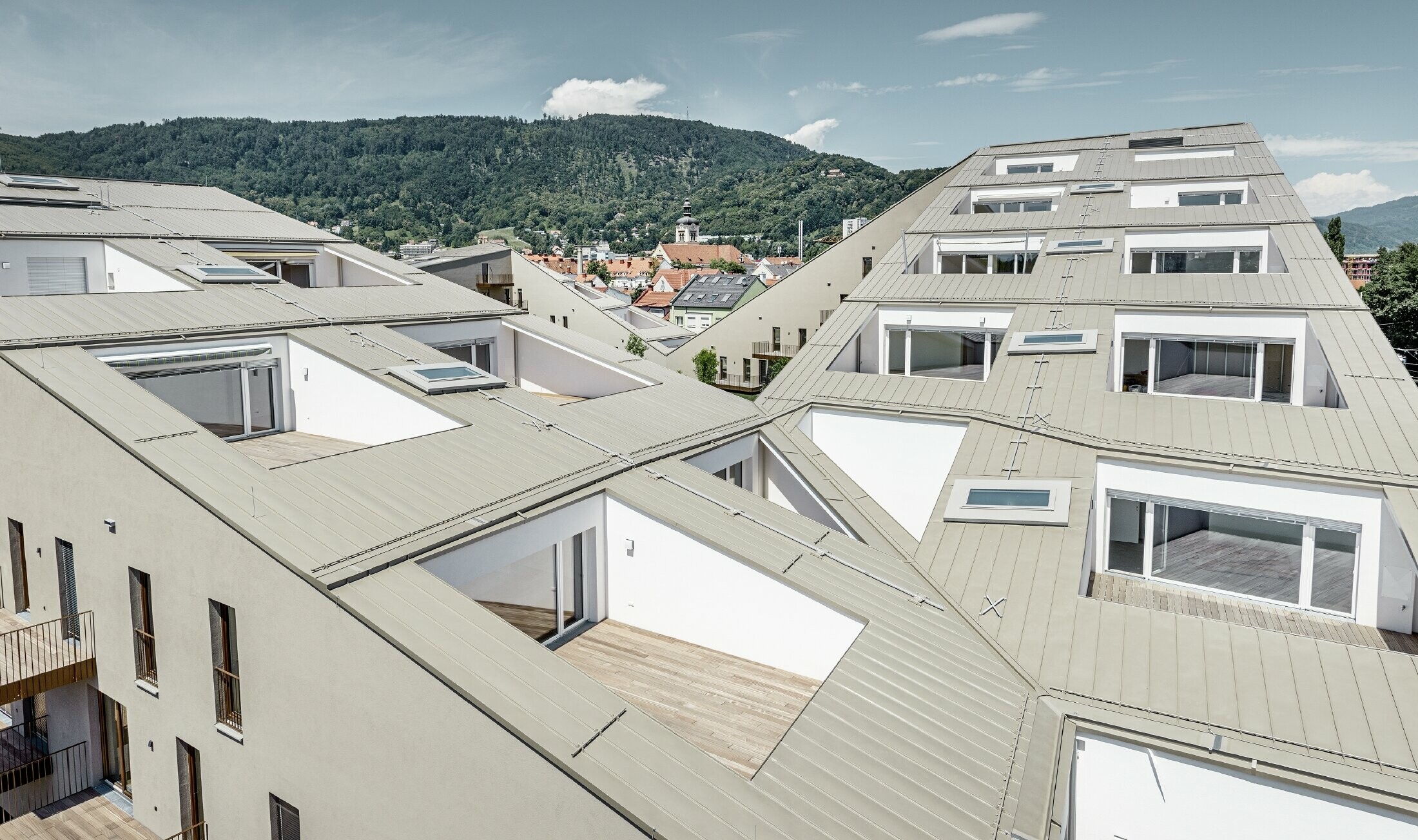 lang gezogene Wohnhausanlage in Graz mit flachen Dachflächen und integrierten Terrassen und großflächigen Fenstern mit einem Prefalzdach in der Sonderfarbe broncemetallic