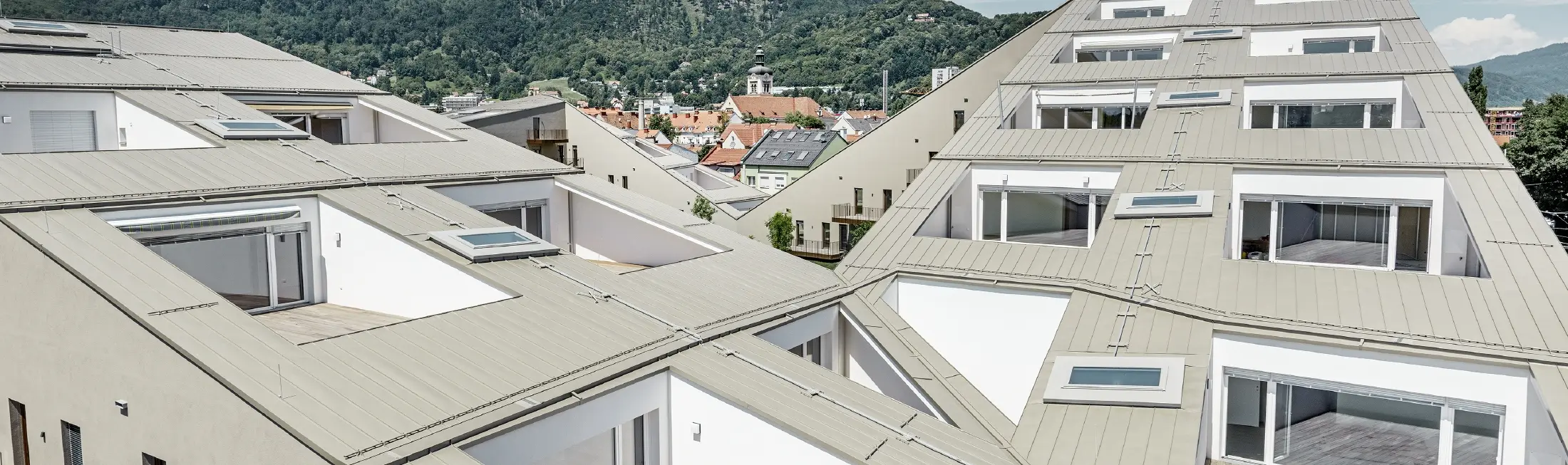 complesso residenziale di forma allungata a Graz con superfici di copertura piane e terrazze integrate e ampie vetrate con una copertura in Prefalz nel colore broncemetallic