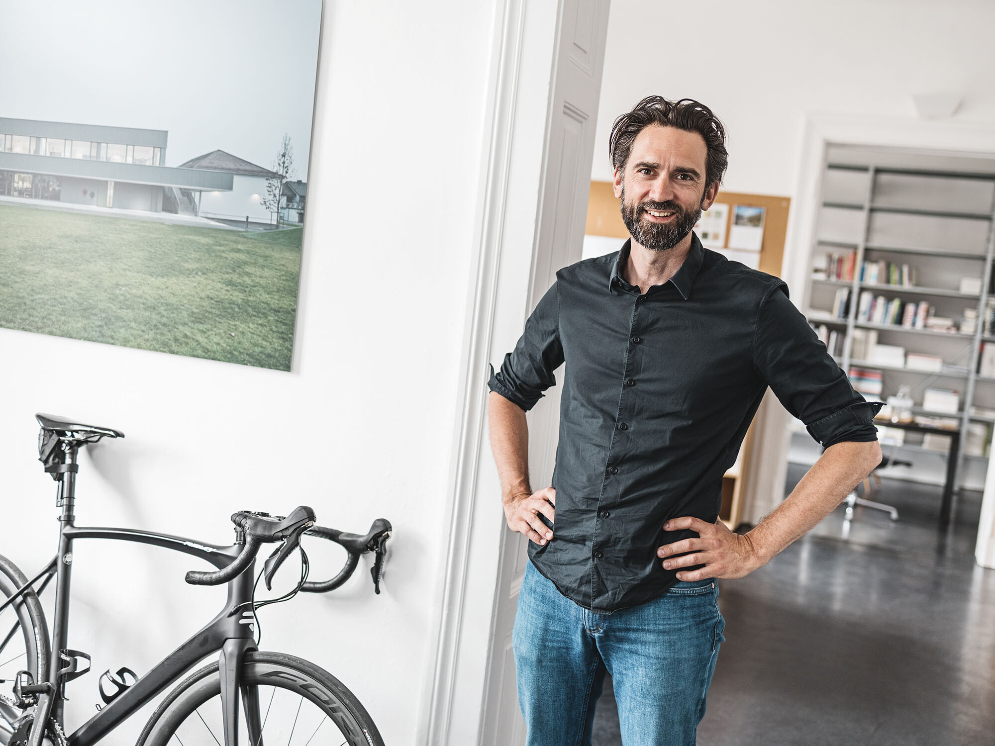 Ritratto dell'architetto Thomas Heil; alle sue spalle un ufficio, mentre accanto a lui vi è una bicicletta appoggiata alla parete.