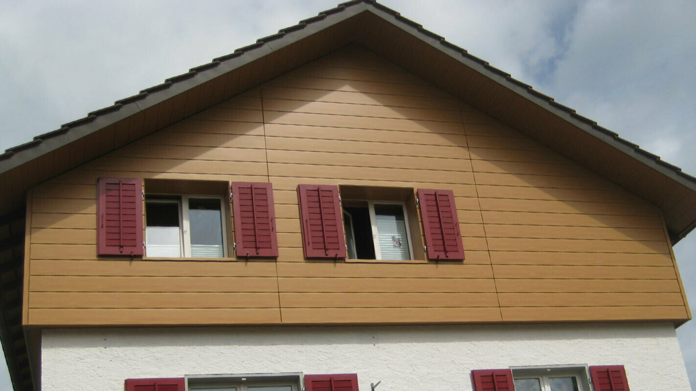 Hausfassade in Holzoptik mit PREFA Sidings horizontal verlegt, Fenster mit roten Fensterläden
