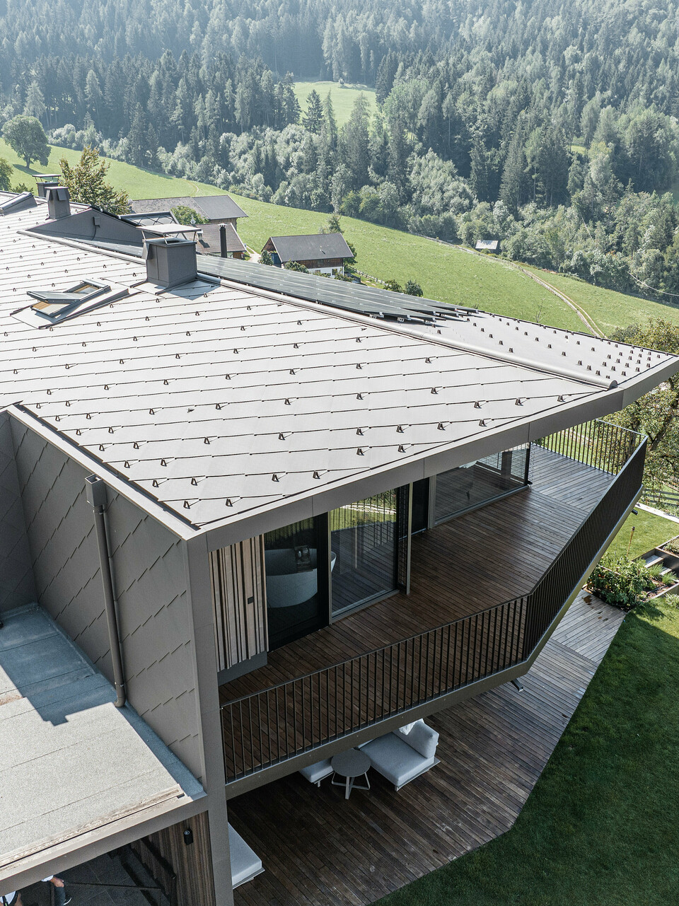 Blick auf eine modernisierte Doppelhaushälfte in Mölten, Südtirol, ausgestattet mit langlebigen PREFA Dach- und Wandrauten 44x44 in P.10 Braun. Die Dach- und Fassadengestaltung kombiniert robustes Aluminium mit Holzelementen, umgeben von einer malerischen Landschaft mit weitem Blick auf bewaldete Hügel. Die Neugestaltung fügt das renovierte Bestandsgebäude und den neu errichteten Standort nahtlos in ein harmonisches Ganzes ein, wobei der Schwerpunkt auf dem Baustoff Holz liegt.