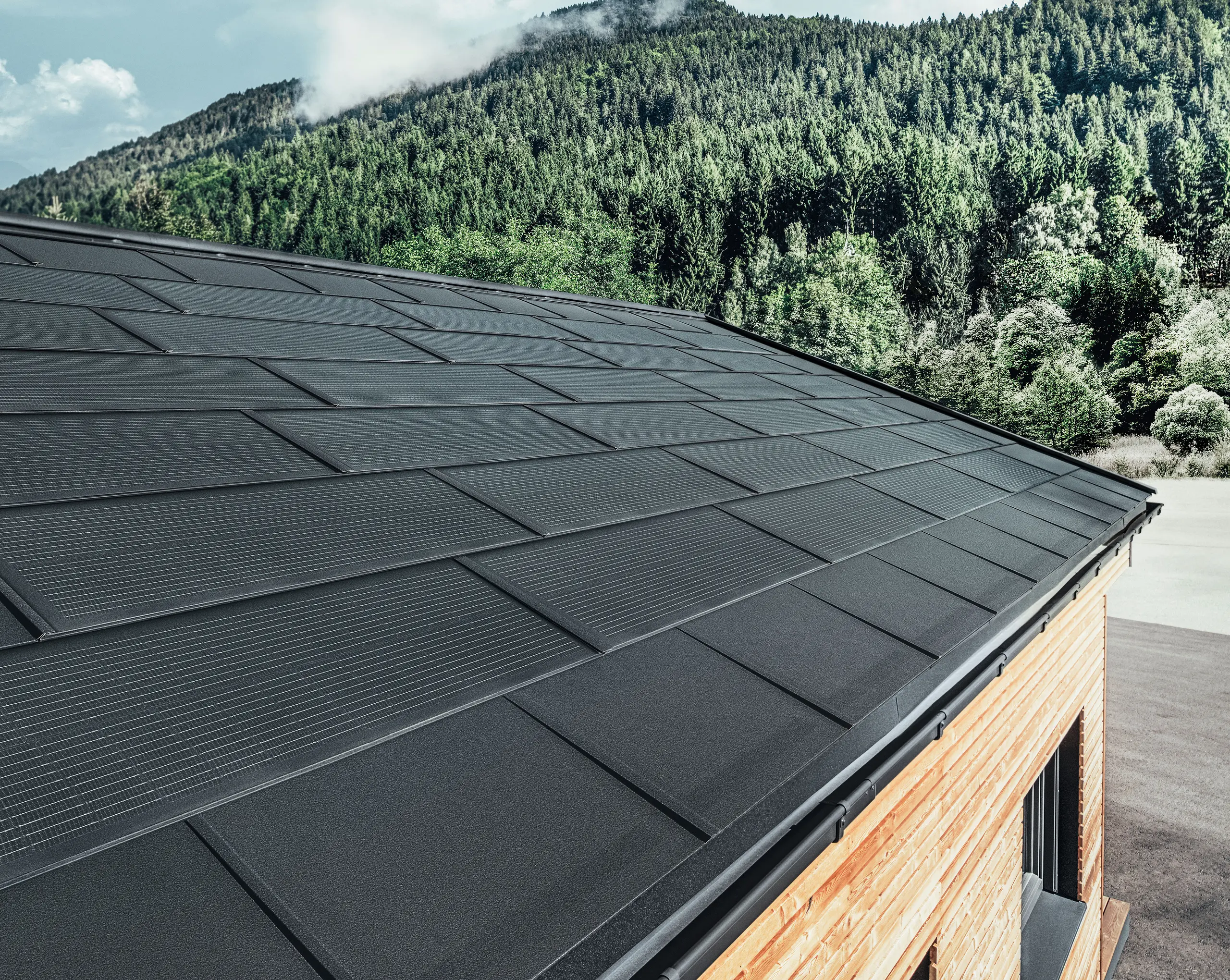 La tegola fotovoltaica PREFA in versione grande abbinata alla tegola R.16 in nero, canale quadro e facciata in larice