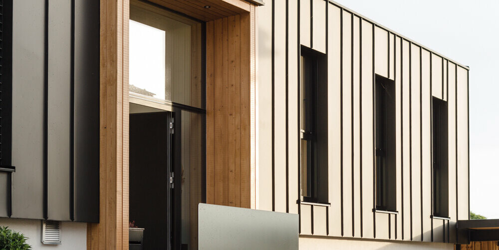Architektonisch anspruchsvolles Einfamilienhaus in Kirchham, Österreich, kunstvoll verkleidet mit langlebigem PREFALZ Aluminium in der eleganten Farbe P.10 Anthrazit von PREFA. Die Fassade zeigt eine harmonische Verbindung von Aluminium und Holz, die für ein zeitgemäßes und ökologisches Wohnkonzept steht. Detailreiche Akzente wie die präzise verarbeiteten Kanten und Falze unterstreichen die handwerkliche Qualität. Die Garage fügt sich mit ihrer schlichten Betonfront und dem minimalistischen Design perfekt in das Gesamtbild ein, während die umliegenden Grünanlagen und die dezente Außenbeleuchtung das Ambiente stilvoll abrunden und zur ästhetischen Ausstrahlung des Gebäudes beitragen.