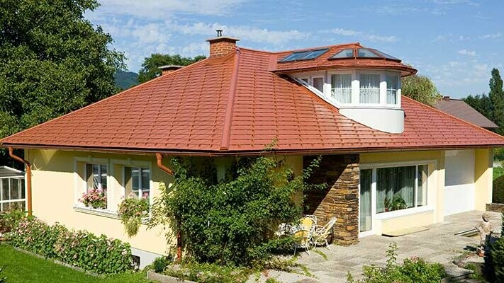 Casa monofamiliare con tetto a padiglione e abbaino rivestita con scandole PREFA con estetica di laterizio nel colore rosso cotto.