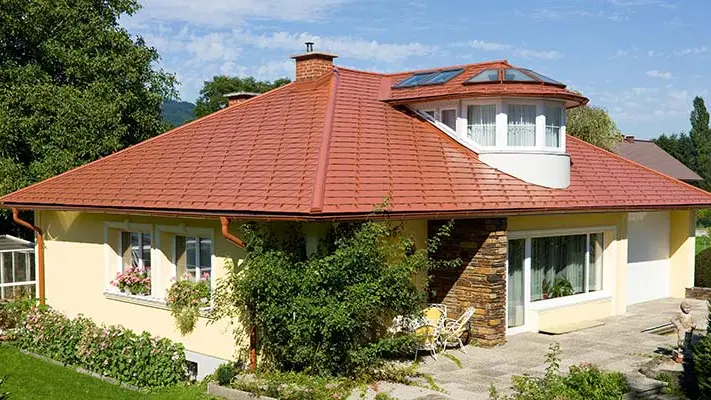 Casa monofamiliare con tetto a padiglione e abbaino rivestita con scandole PREFA con estetica di laterizio nel colore rosso cotto.
