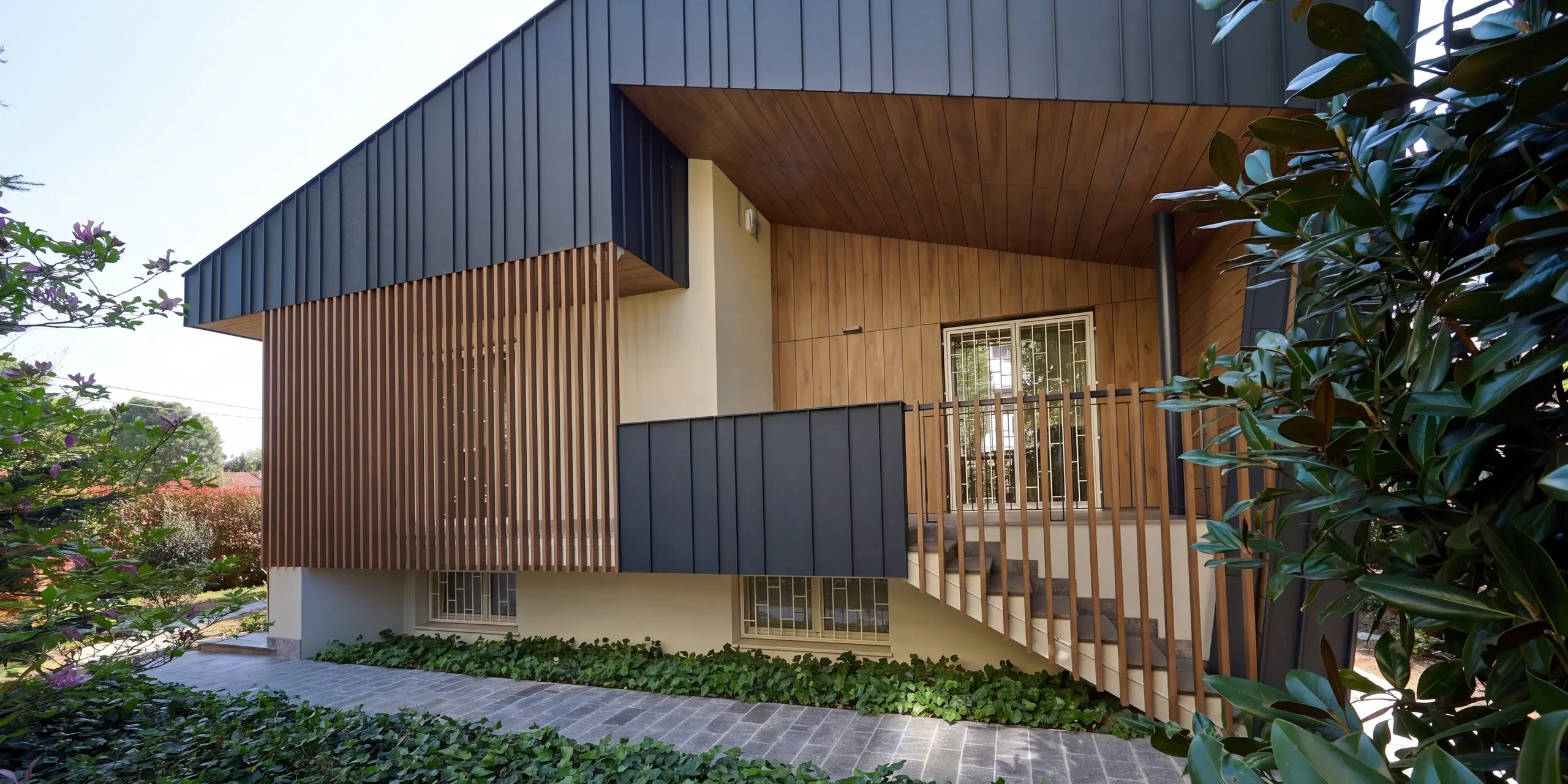 Nahaufnahme der Villa Castellanza mit einer hochwertigen PREFALZ Aluminiumfassade in der Farbe P.10 Anthrazit. Die markanten Stehfalze, die warmen Holzelemente und die großzügige Überdachung schaffen einen spannenden architektonischen Kontrast. PREFA Aluminium verleiht der Gebäudehülle eine elegante Optik, eine hohe Witterungsbeständigkeit sowie eine langlebige Qualität bei minimalem Wartungsaufwand.