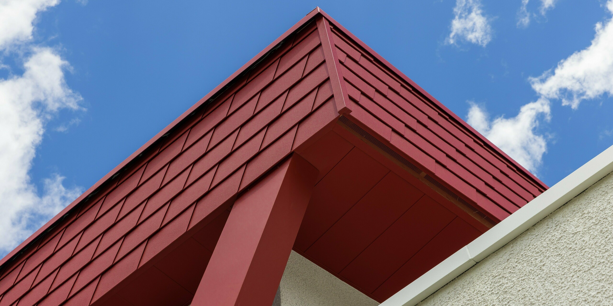 Detailaufnahme der Fassade des Summit Mountain Clubs in Ratschings mit robusten PREFA Wandschindeln in der Farbe P.10 Oxydrot und einem markanten roten Stützträger. Die hochwertige PREFA Blechfassade ist nicht nur optisch ansprechend, sondern bietet auch langfristigen Schutz gegen die Herausforderungen des alpinen Klimas.