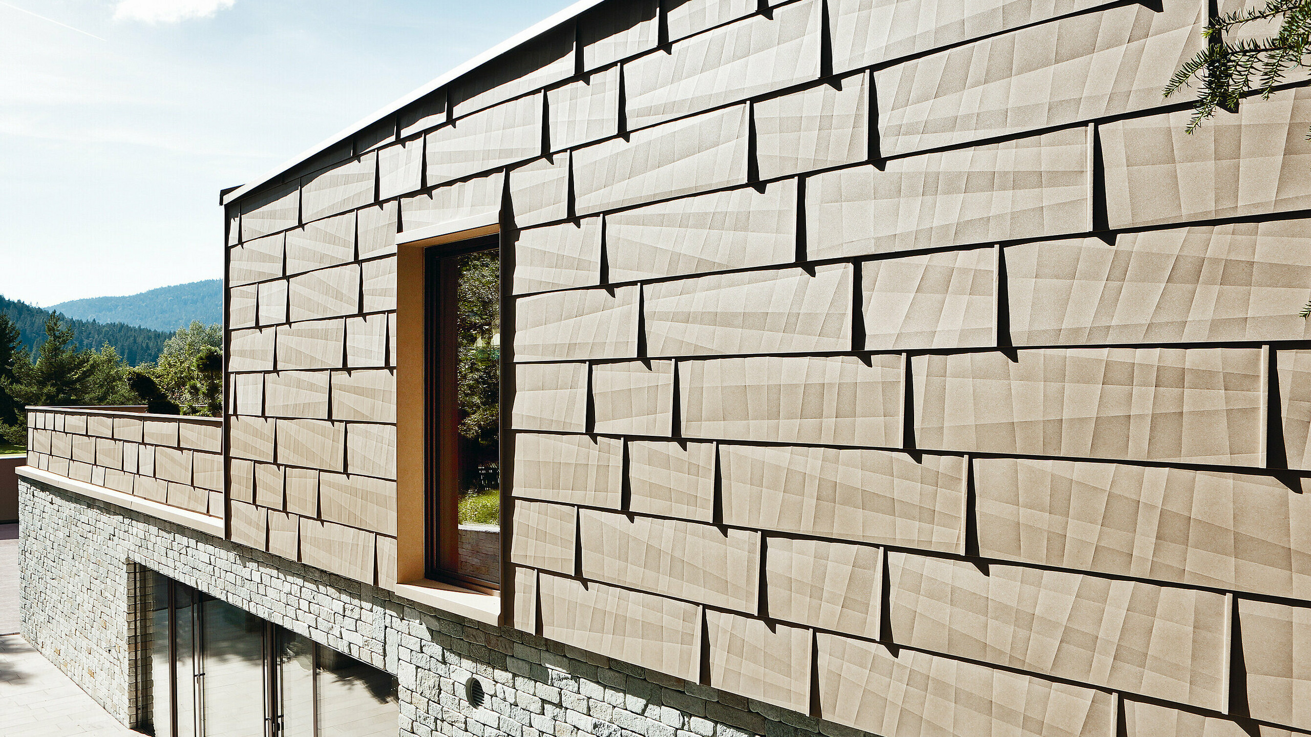 Kombination von Aluminium- und Steinfassade An dieser Außenfassade wurde das PREFA Fassadenpaneel FX.12 in P.10 Sandbraun mit einer Steinfassade im Untergeschoß kombiniert.