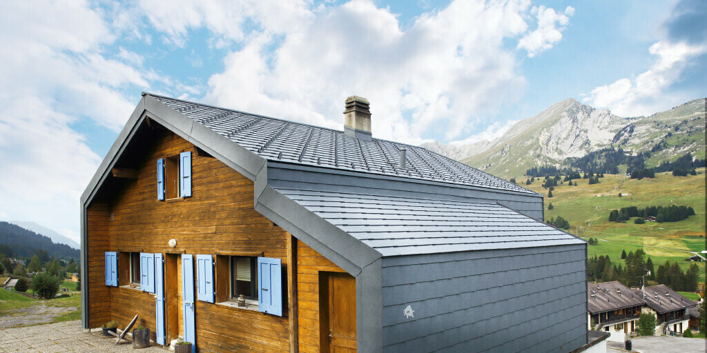 Casa di montagna in Svizzera con facciata in legno abbinata a tetto e scaglie per facciata PREFA in grigio pietra