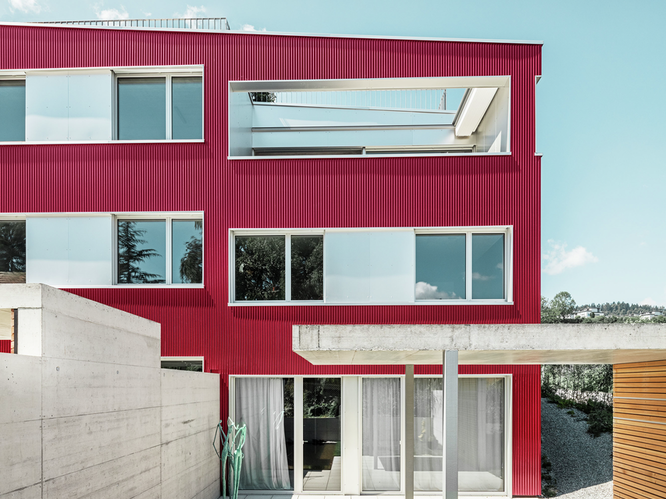 Vista frontale di un edificio residenziale sul Lago di Zurigo in Svizzera sotto il sole e il cielo blu, rivestito con il profilo ondulato PREFA nel colore rosso vino