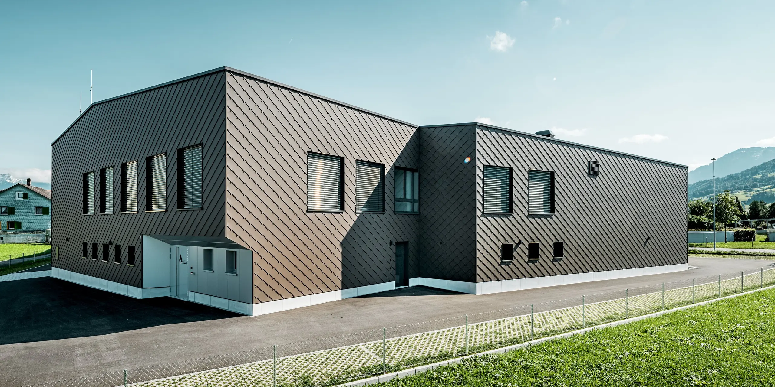 Rückansicht des Infrastrukturgebäudes der Feuerwehr und des Elektrizitätswerks in Wangen, Schweiz, mit durchgängiger Fassadenbekleidung aus PREFA Wandrauten 29 × 29 in der Farbe P.10 Braun. Die präzise Rautenstruktur umhüllt die kubische Gebäudeform und verleiht ihr eine moderne, hochwertige Erscheinung. Die langlebige Aluminiumfassade überzeugt durch hohe Witterungsbeständigkeit, geringen Wartungsaufwand und maximale Gestaltungsfreiheit für anspruchsvolle Architektur.