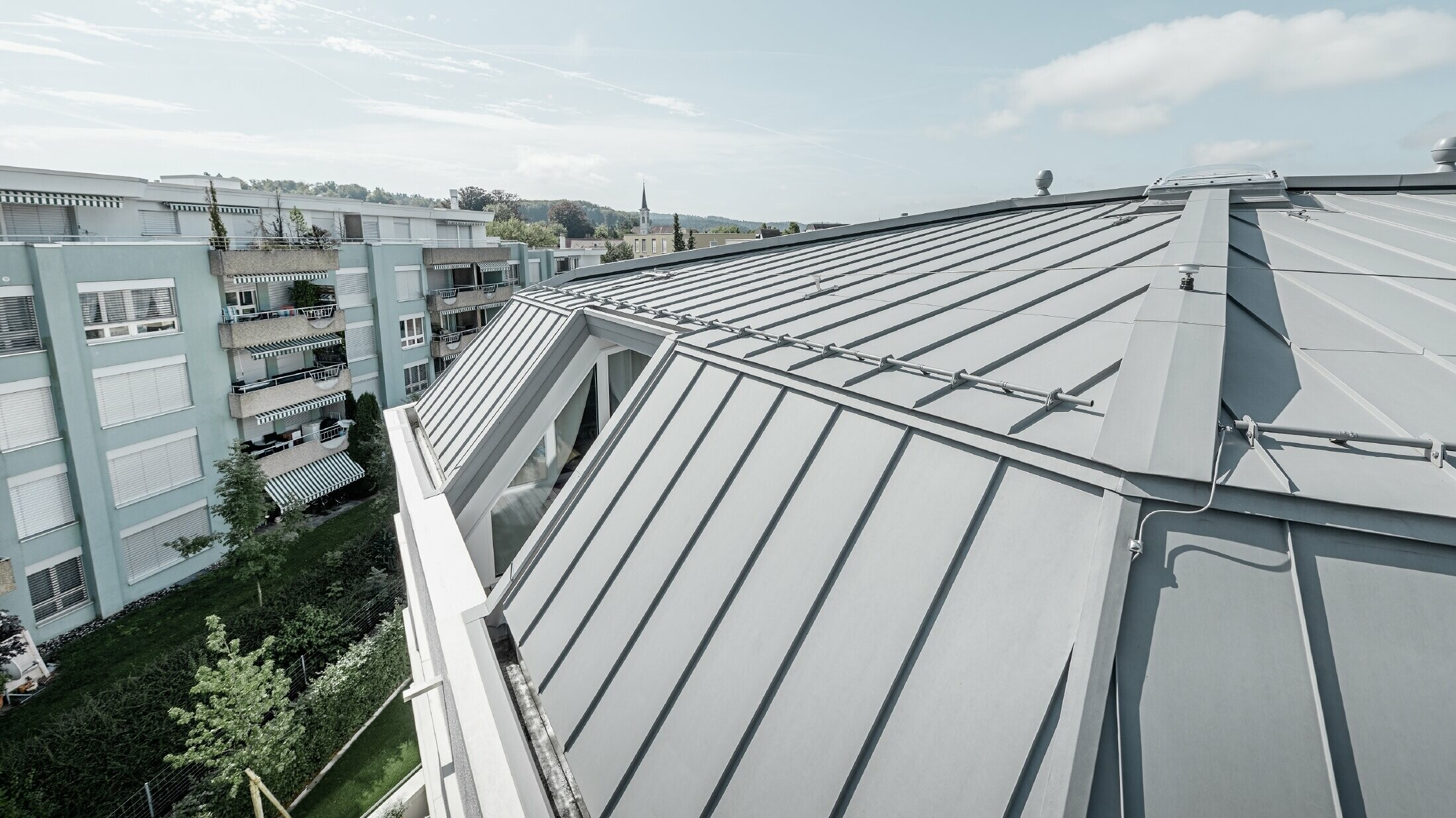 Immagine dettagliata della superficie del tetto di un condominio; tetto con aggraffatura realizzato con Prefalz PREFA in grigio patina.
