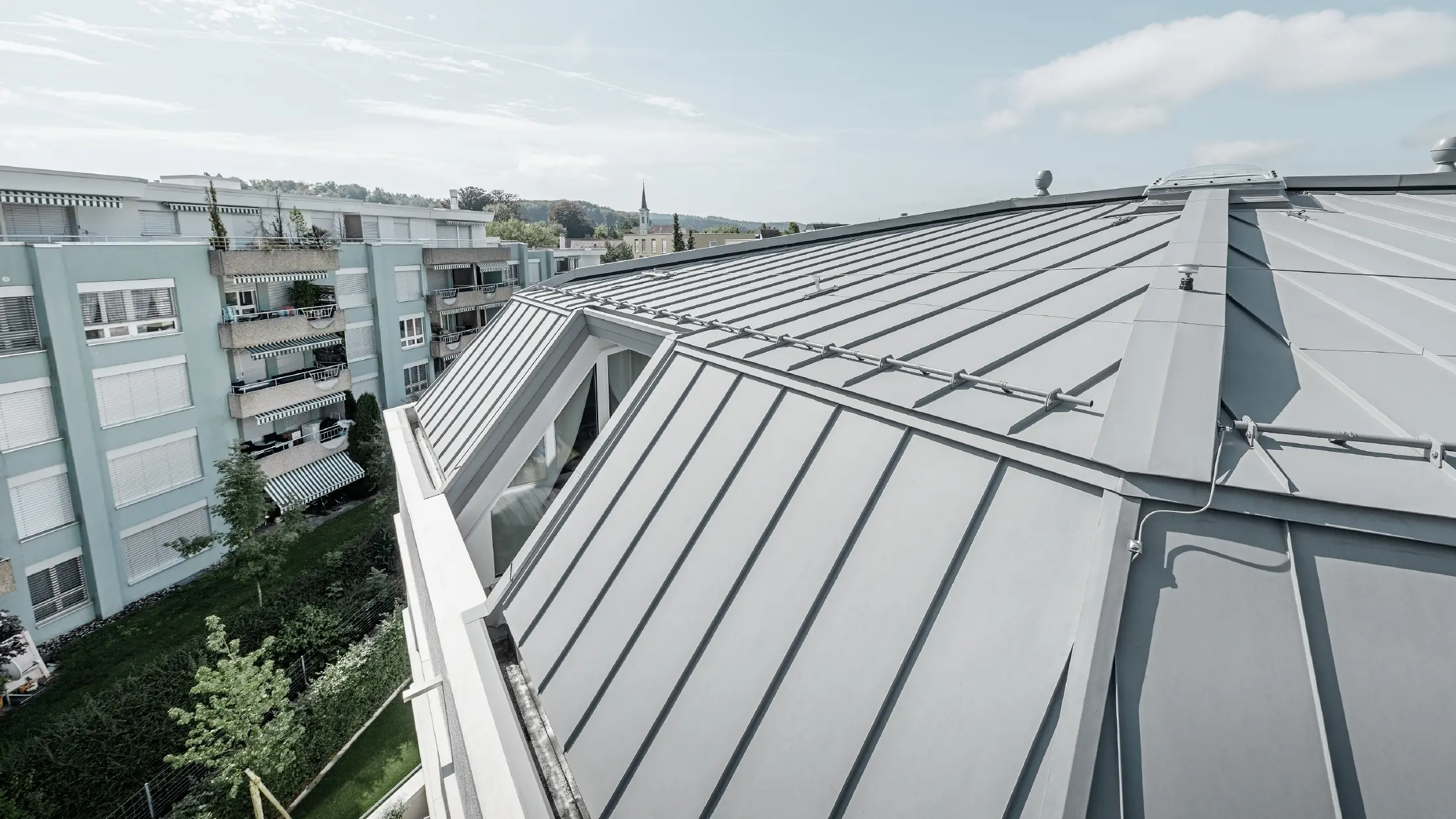 Immagine dettagliata della superficie del tetto di un condominio; tetto con aggraffatura realizzato con Prefalz PREFA in grigio patina.