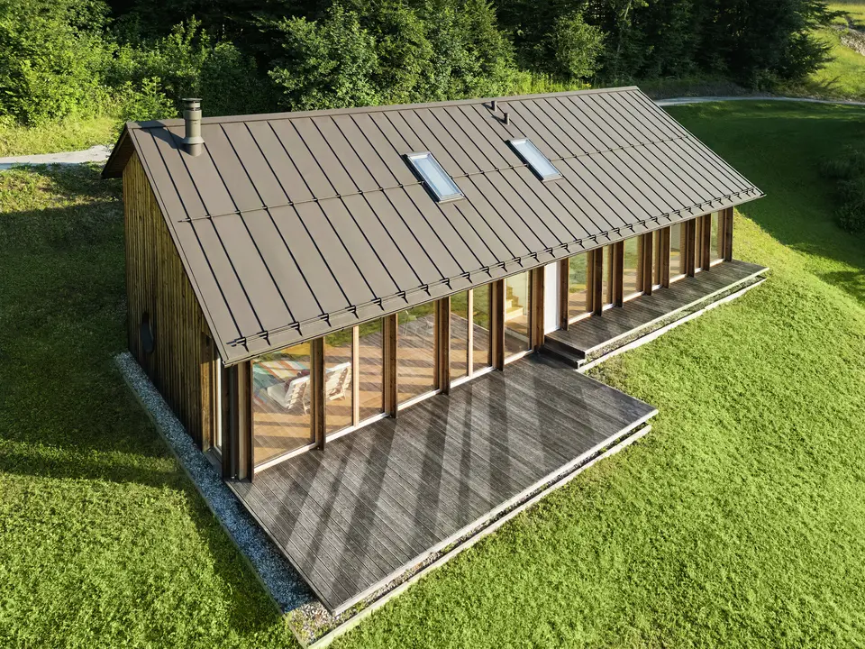 Ein modernes Holzhaus mit großzügiger Glasfassade und einem robusten PREFALZ-Aluminiumdach in der Farbe P.10 Braun – ideal für Hanglagen wie in Vinje. Die hochwertige Dachdeckung garantiert maximale Witterungsbeständigkeit, lange Lebensdauer und eine elegante Optik. Präzise gesetzte Stehfalze und integrierte Dachfenster schaffen ein luftiges und nachhaltiges Wohnkonzept. Die präzise Verarbeitung der Aluminium-Stehfalze wird aus der Vogelperspektive sichtbar.