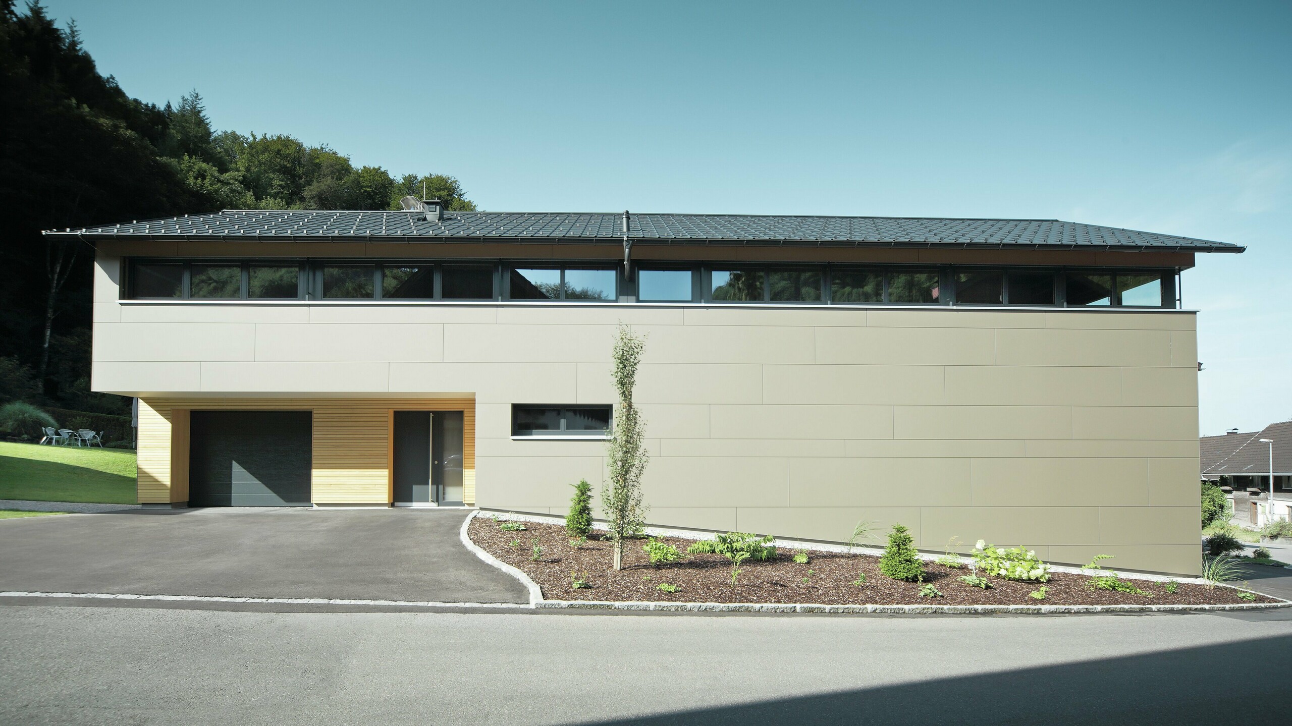 Casa lunga con pannello di copertura PREFA in P.10 antracite, combinato con pannello composito PREFA in bronzo sulla facciata; stile di costruzione moderno combinato con finestre strette e facciata in legno