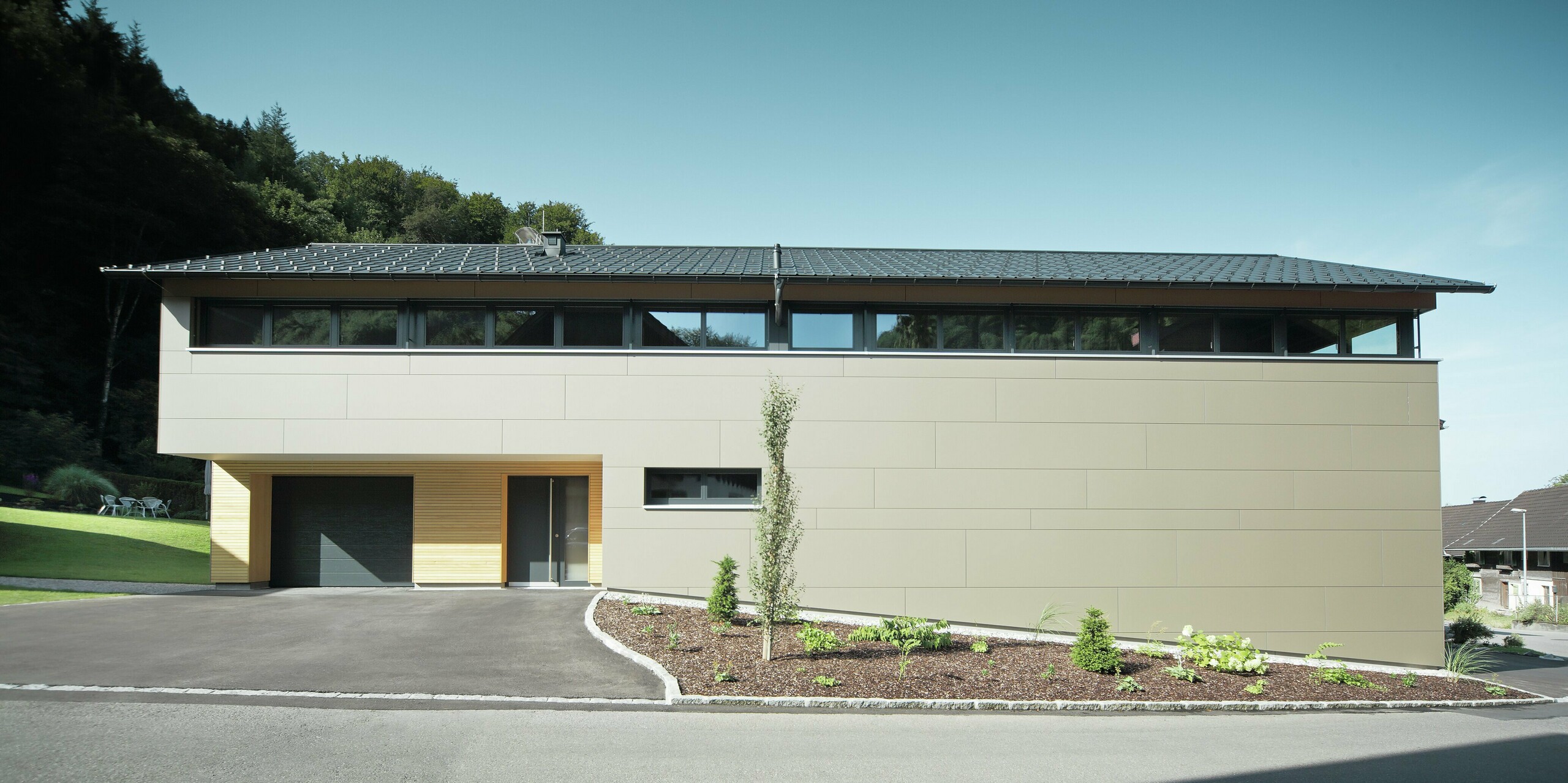 Casa lunga con pannello di copertura PREFA in P.10 antracite, combinato con pannello composito PREFA in bronzo sulla facciata; stile di costruzione moderno combinato con finestre strette e facciata in legno