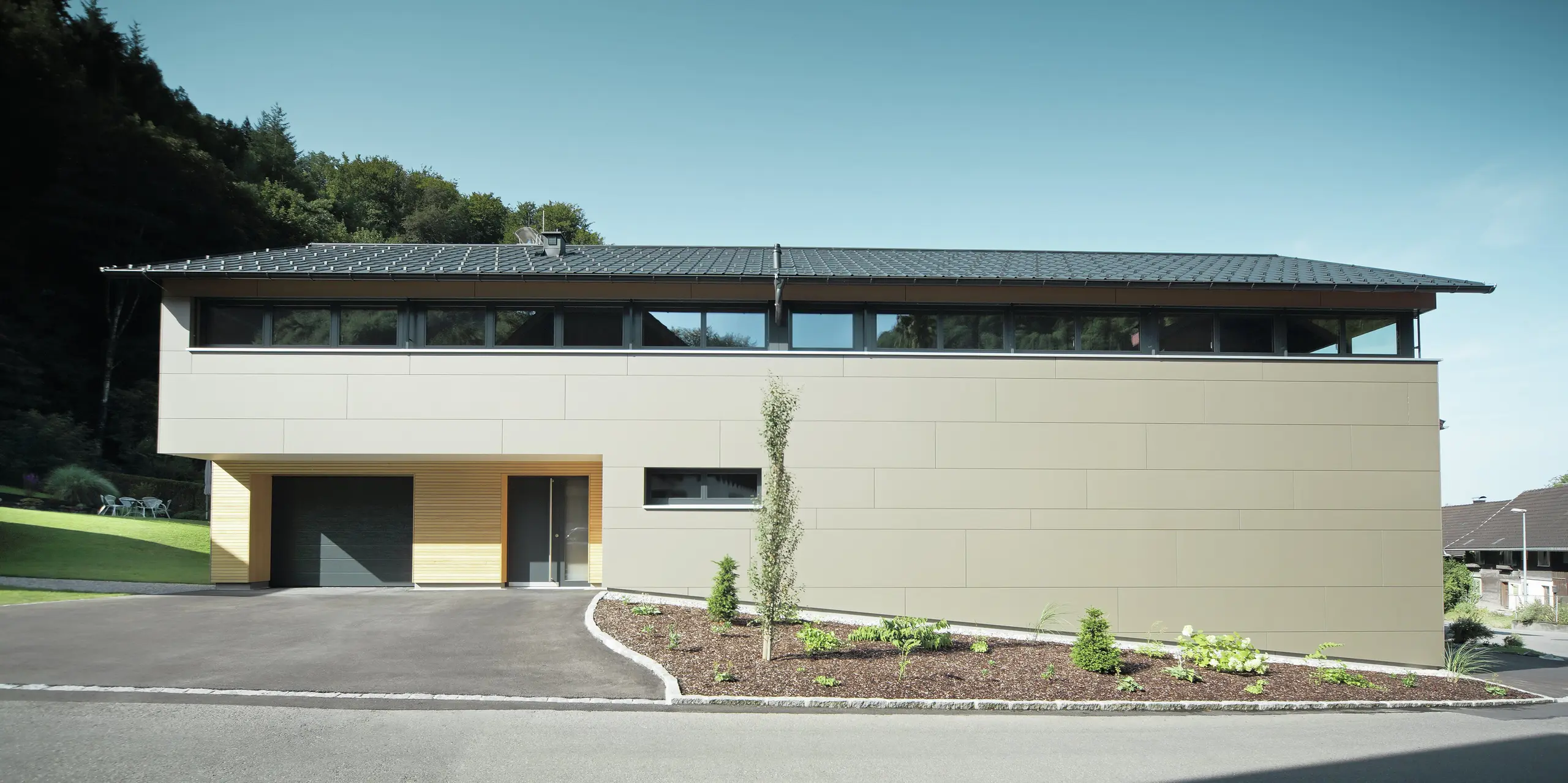 Casa lunga con pannello di copertura PREFA in P.10 antracite, combinato con pannello composito PREFA in bronzo sulla facciata; stile di costruzione moderno combinato con finestre strette e facciata in legno