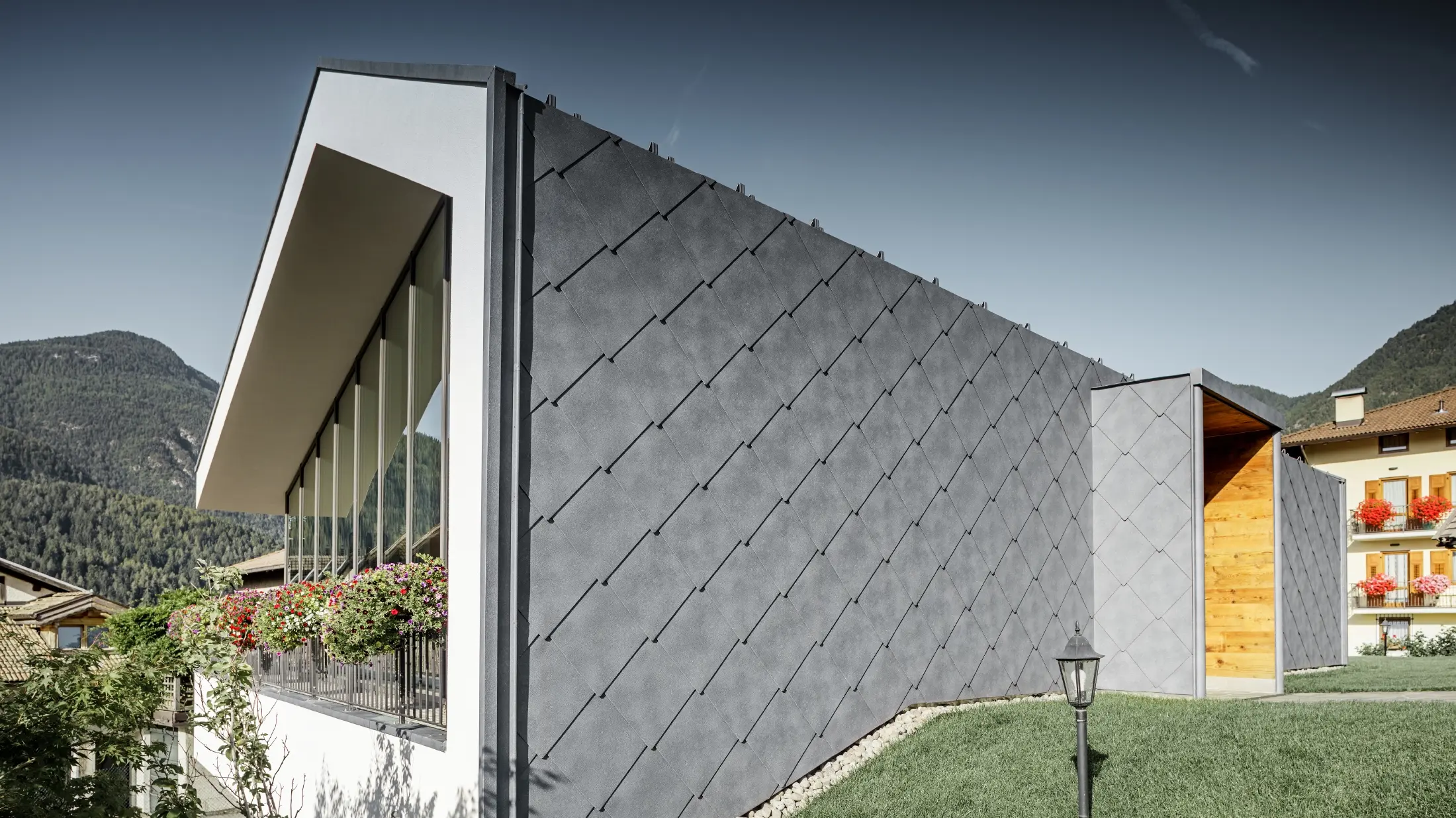 Moderno salone da parrucchiere a Livo rivestito con scaglia 44 di copertura e per facciata in grigio pietra di PREFA