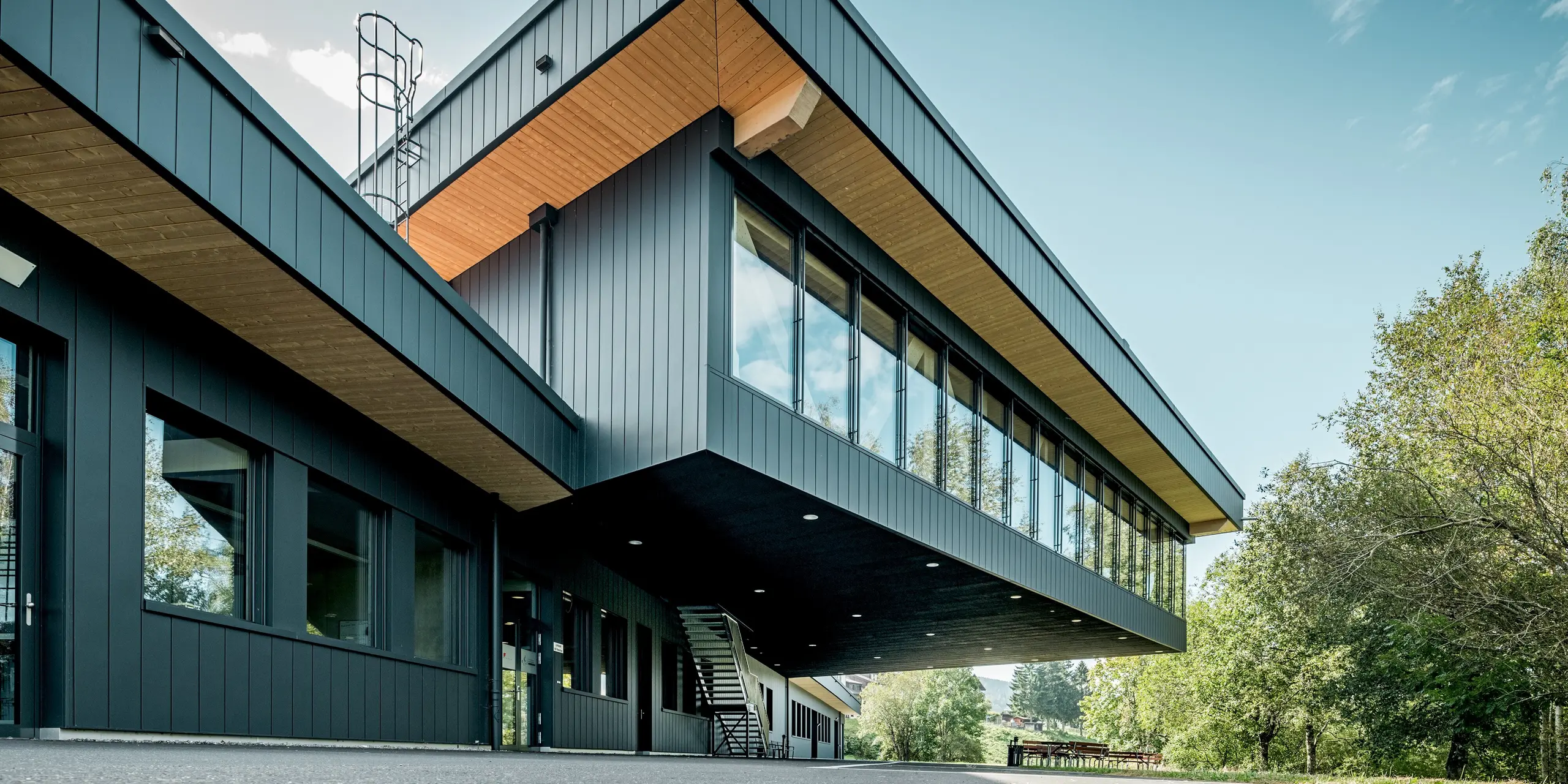 Modernes Firmengebäude von KIF Parechoc in Le Brassus mit eindrucksvoll auskragendem Obergeschoss und vertikal verlegten PREFA Sidings in P.10 Anthrazit. Die markante Aluminiumfassade bildet gemeinsam mit den großflächigen Verglasungen und warmen Holzuntersichten einen spannenden Kontrast. PREFA Sidings überzeugen durch Langlebigkeit, Korrosionsbeständigkeit und ihre besonders wartungsarme Oberfläche.