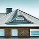 Einfamilienhaus aus den 70ern mit einem Schindeldach aus Aluminium in P.10 Steingrau mit geschwungener Gaube mit rundem Fenster