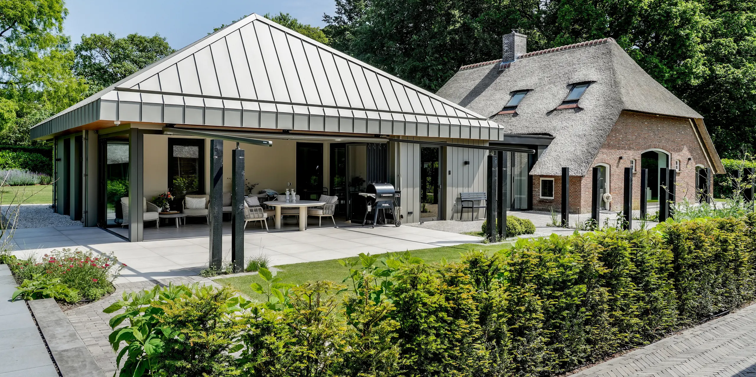 Der moderne PREFALZ Anbau in Putten bildet einen faszinierenden Kontrast zum traditionellen Reetdachhaus. Die elegante Aluminiumhülle in P.10 Prefabronze, markante Winkelstehfalze, großzügige Verglasungen und die offene Terrasse schaffen einen architektonischen Blickfang. PREFA Aluminium überzeugt durch langlebige Qualität, hohe Witterungsbeständigkeit und die harmonische Verbindung von moderner Baukultur und historischem Bestand.