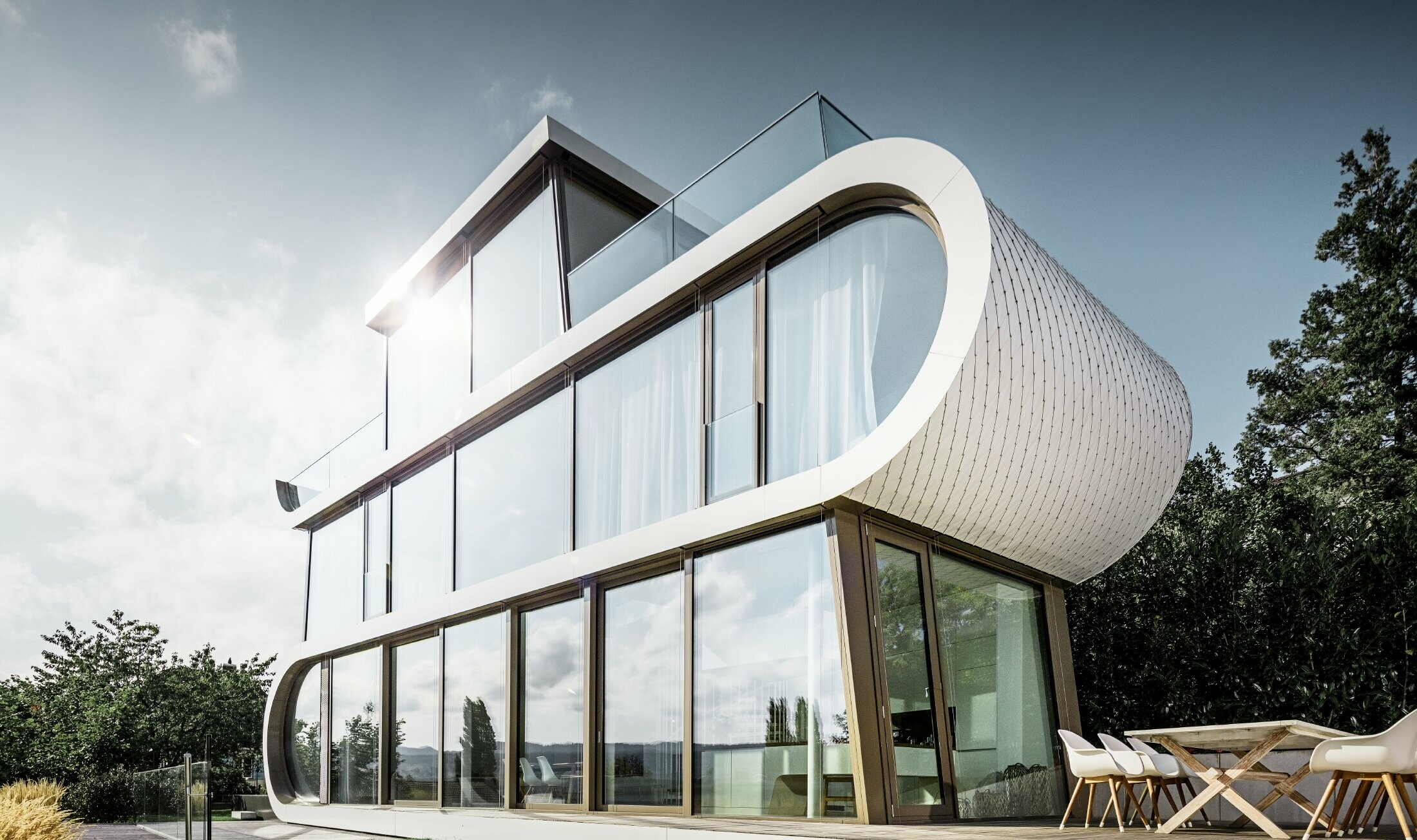 Moderna casa unifamiliare progettata dall'architetto Camenzind; una fascia ricurva collega i livelli, all'esterno l'arco è rivestito con le scaglie PREFA, facili da lavorare, in bianco puro.