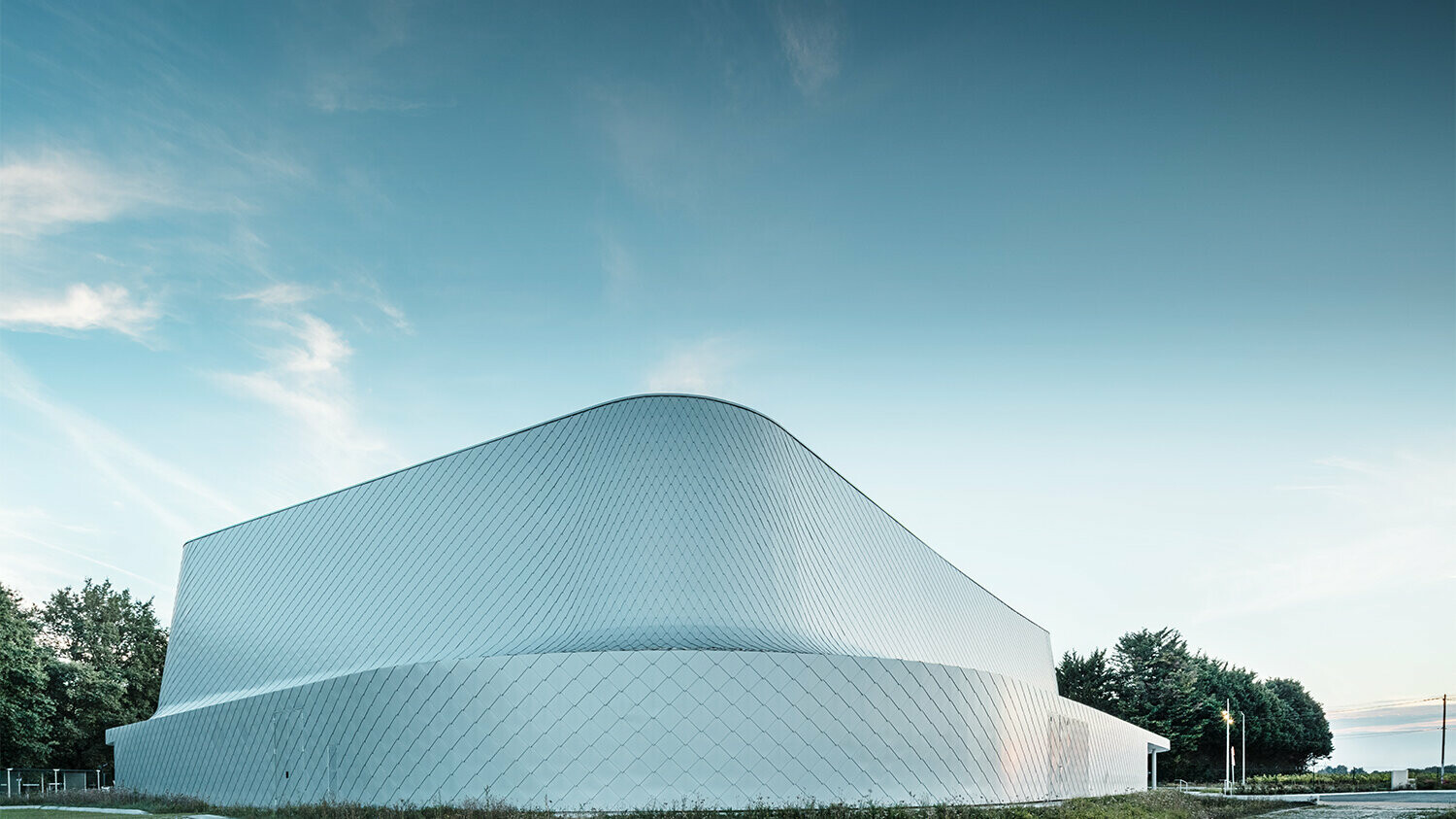 Hintere Seite der monochromen Halle mit Begrünung und einem angrenzenden Weg.