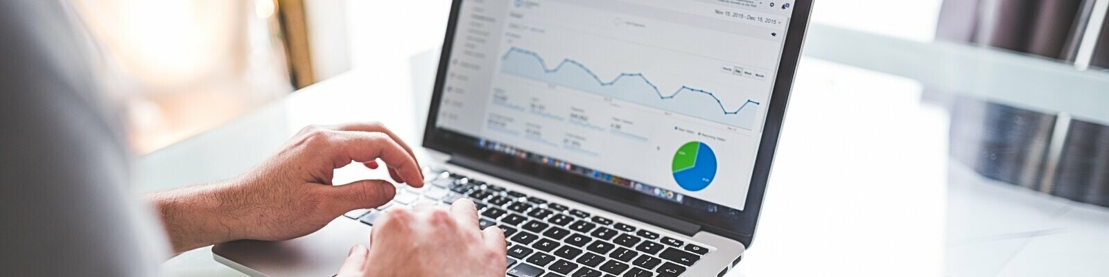 Una persona che lavora su un laptop con sullo schermo rappresentazioni grafiche di statistiche e un diagramma circolare, che indicano lo svolgimento di attività di marketing online.