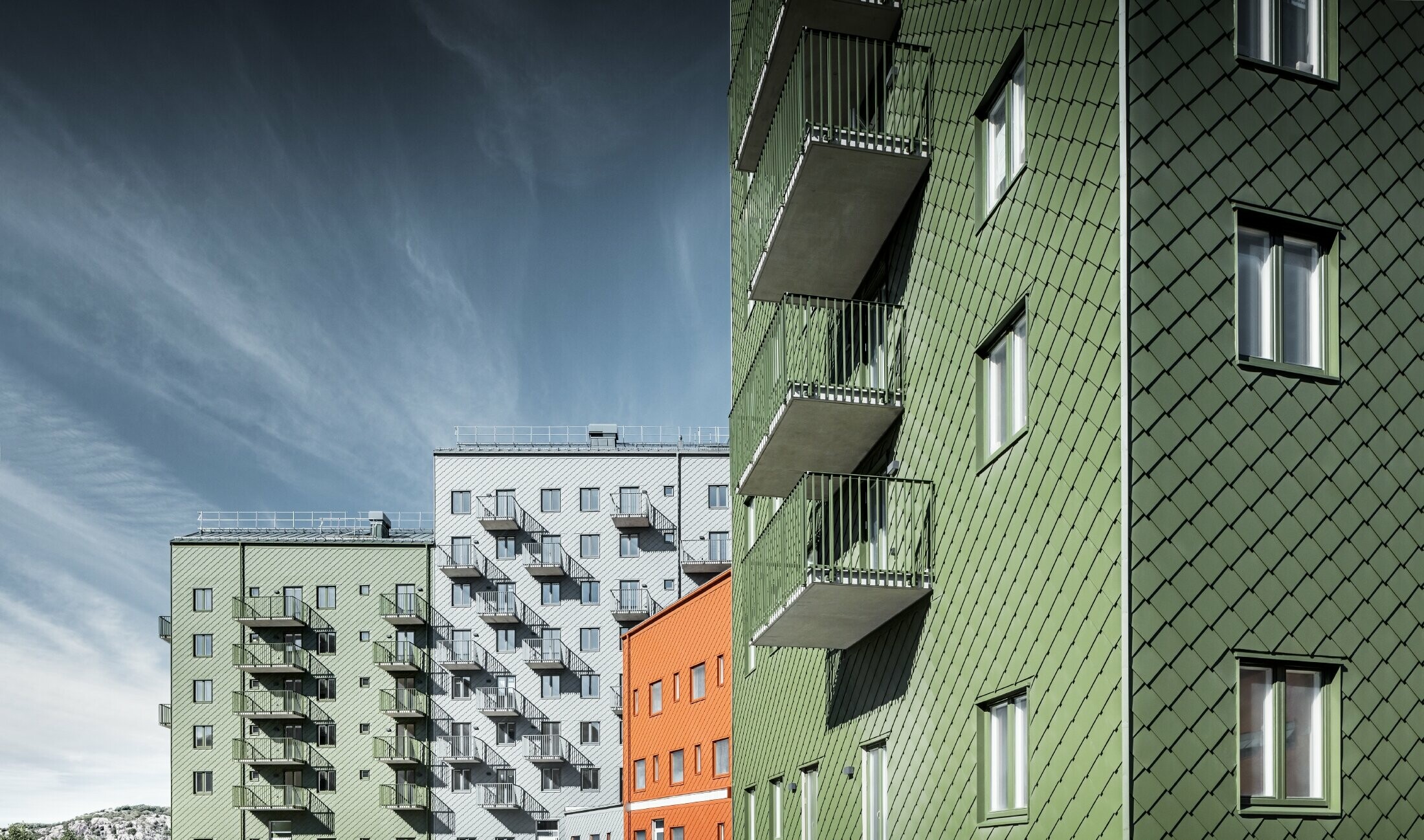 Diverse abitazioni l’una accanto all’altra, rivestite con la scaglia 29 x 29 PREFA nei colori rosso cotto, verde oliva e grigio chiaro.
