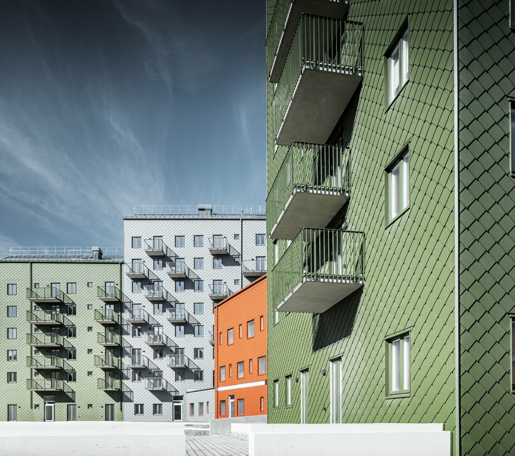 Diverse abitazioni l’una accanto all’altra, rivestite con la scaglia 29 x 29 PREFA nei colori rosso cotto, verde oliva e grigio chiaro.