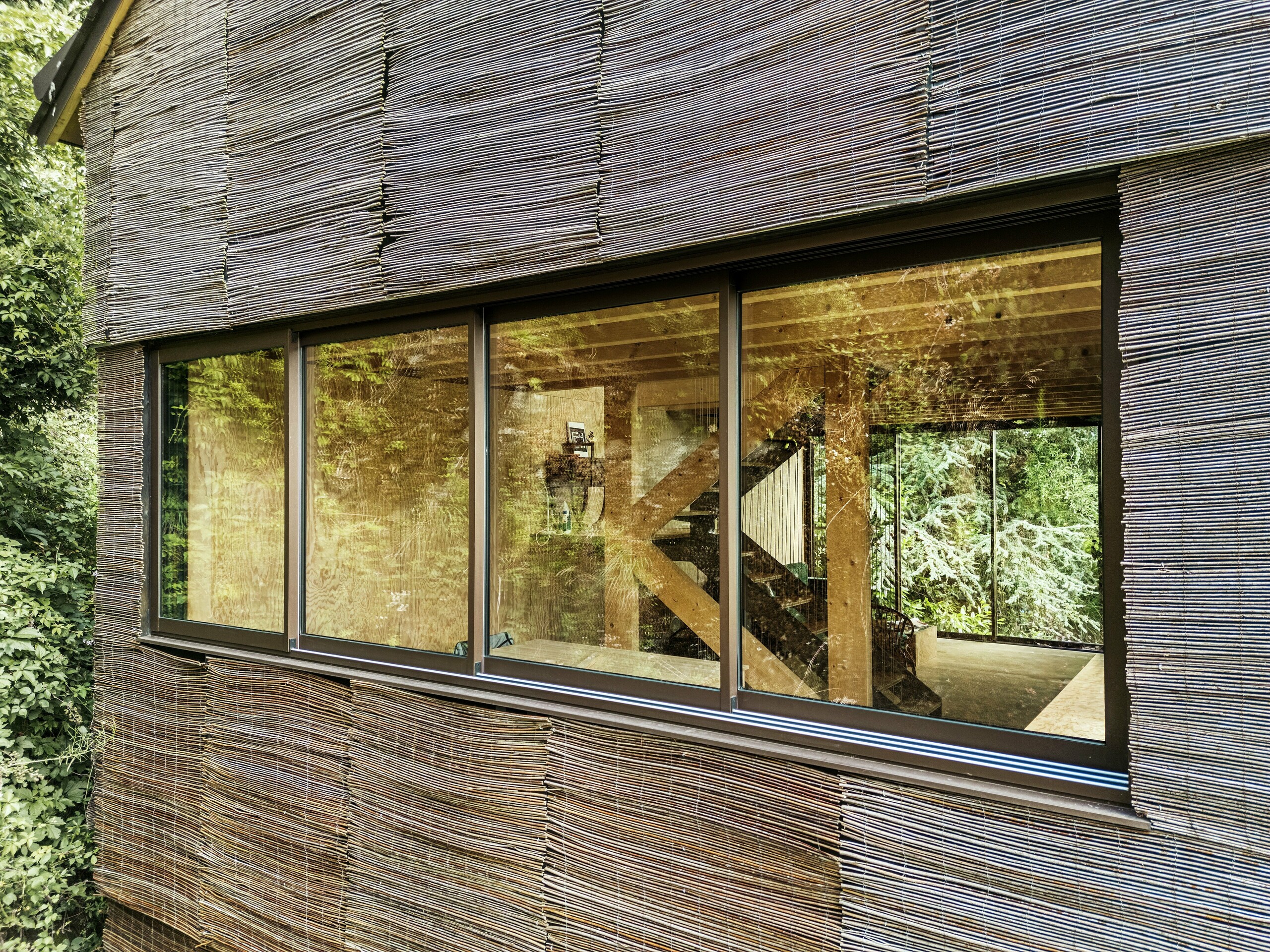 Primo piano di una finestra con telaio moderno in alluminio e facciata in salice su una casa in Francia - design sostenibile con scandole PREFA e ambiente naturale.