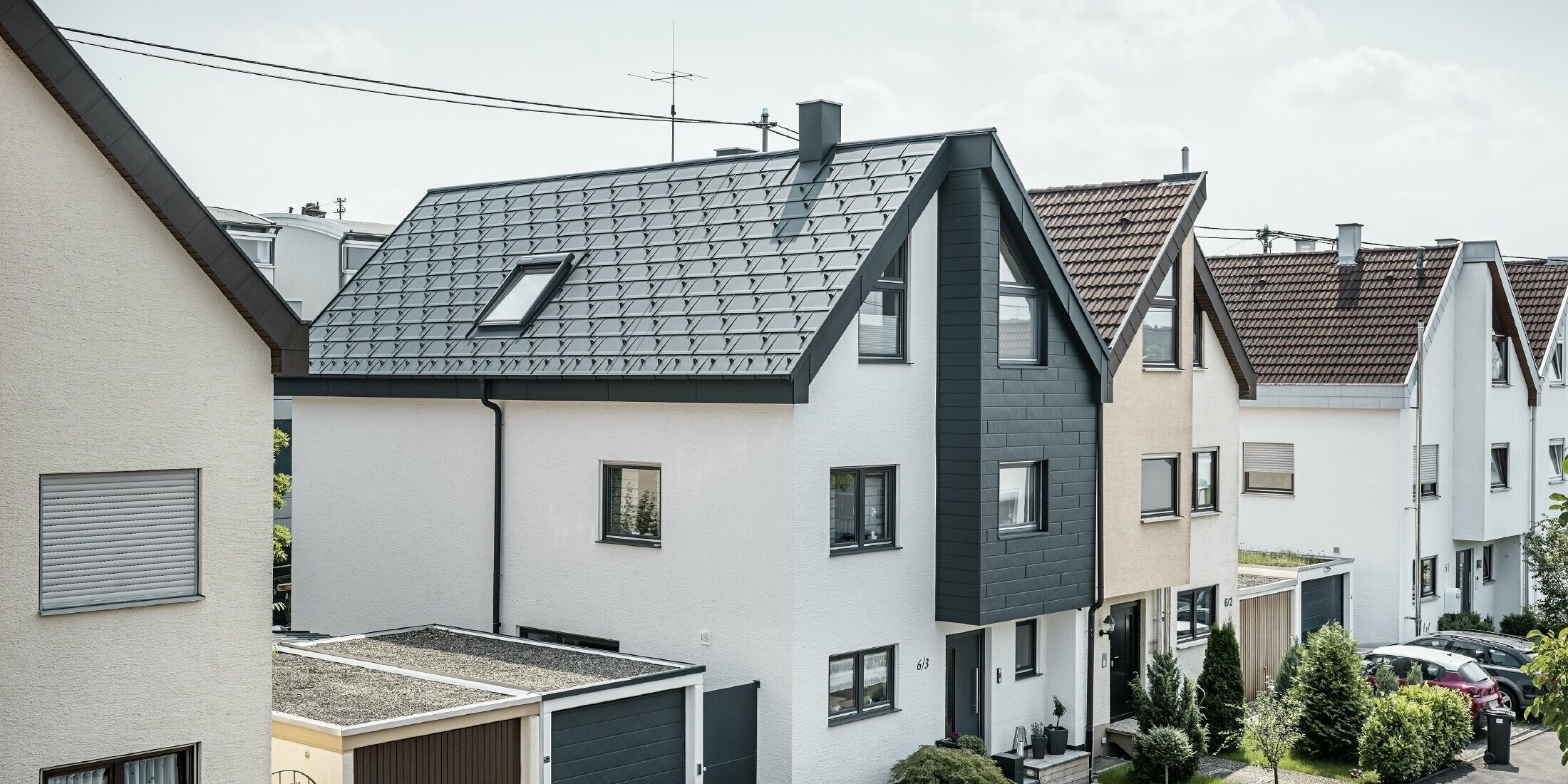 Una casa bifamiliare è già stata ristrutturata, con una fresca facciata in intonaco bianco abbinata a una facciata PREFA Doga.X color antracite. Il tetto è stato ricoperto con la tegola PREFA R.16. Lo smaltimento delle acque piovane avviene tramite un canale quadro angolare con tubo pluviale PREFA.