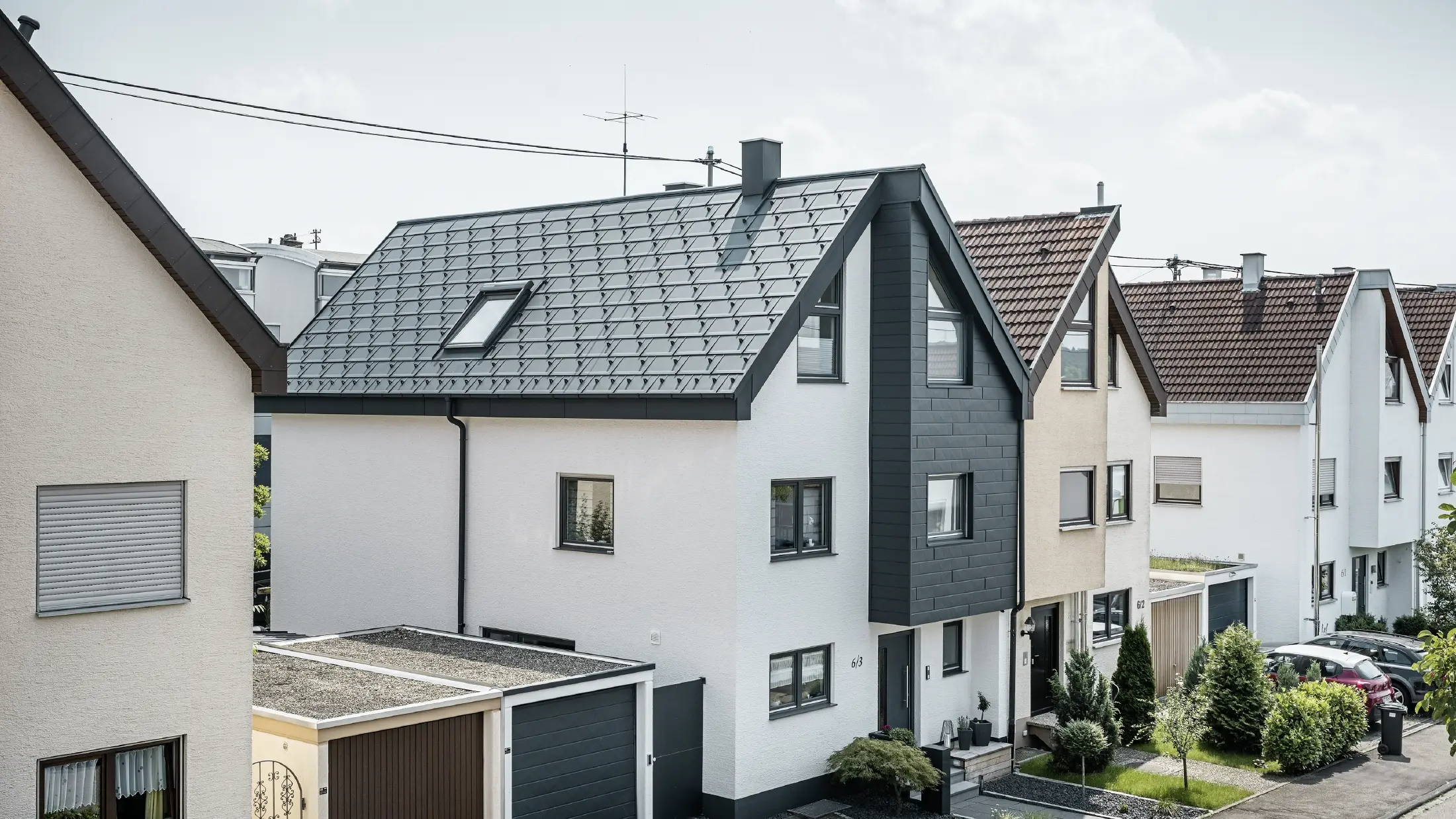 Una casa bifamiliare è già stata ristrutturata, con una fresca facciata in intonaco bianco abbinata a una facciata PREFA Doga.X color antracite. Il tetto è stato ricoperto con la tegola PREFA R.16. Lo smaltimento delle acque piovane avviene tramite un canale quadro angolare con tubo pluviale PREFA.