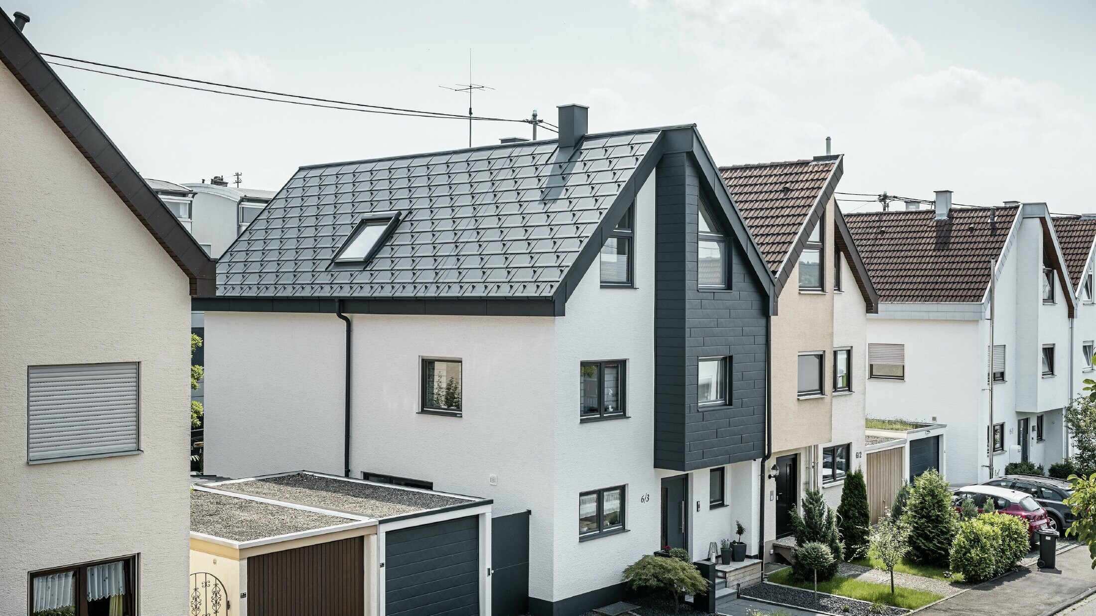 Una casa bifamiliare è già stata ristrutturata, con una fresca facciata in intonaco bianco abbinata a una facciata PREFA Doga.X color antracite. Il tetto è stato ricoperto con la tegola PREFA R.16. Lo smaltimento delle acque piovane avviene tramite un canale quadro angolare con tubo pluviale PREFA.